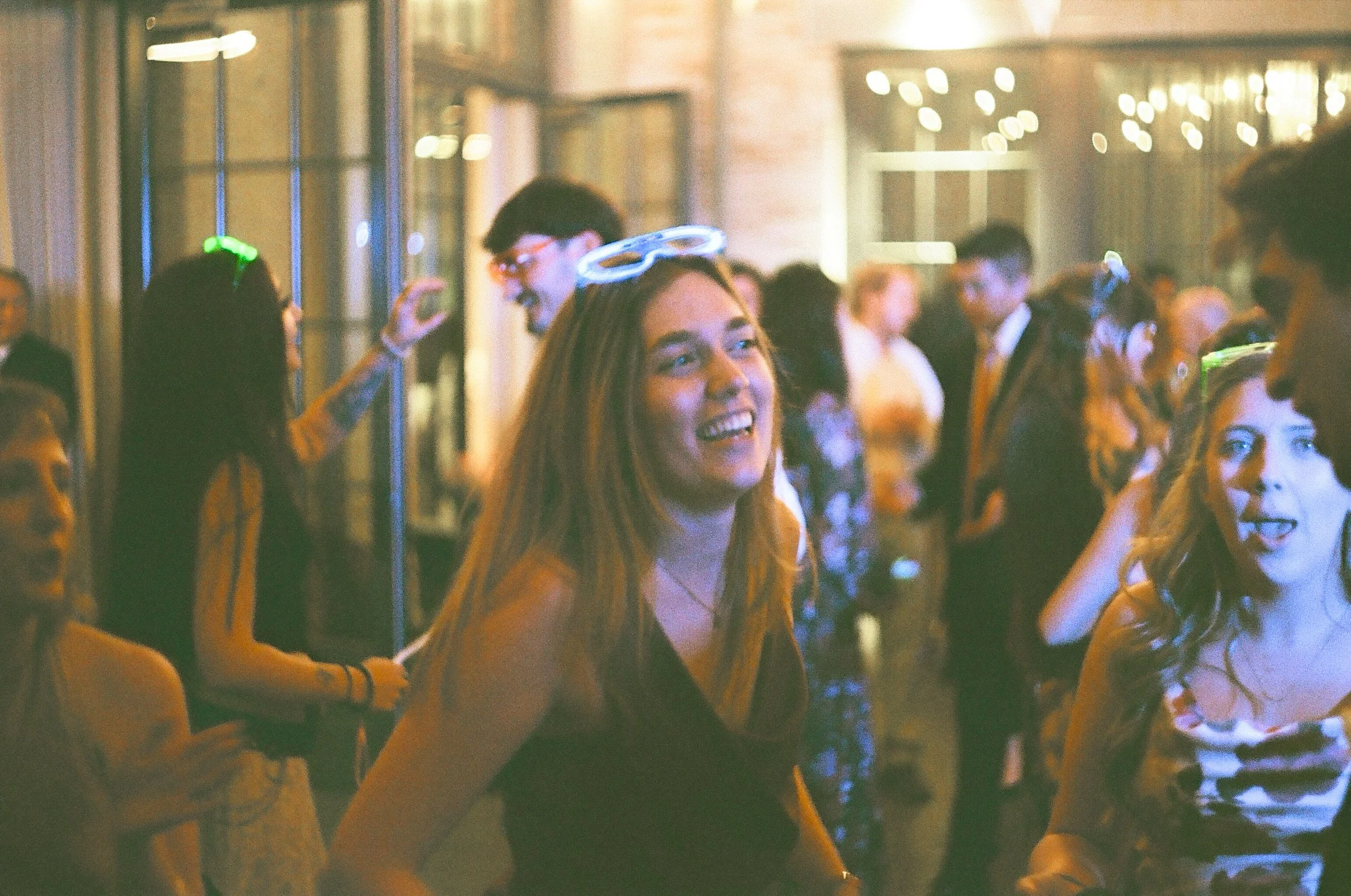 People at a lively indoor event, with some wearing glow-in-the-dark accessories, smiling and engaging with each other.