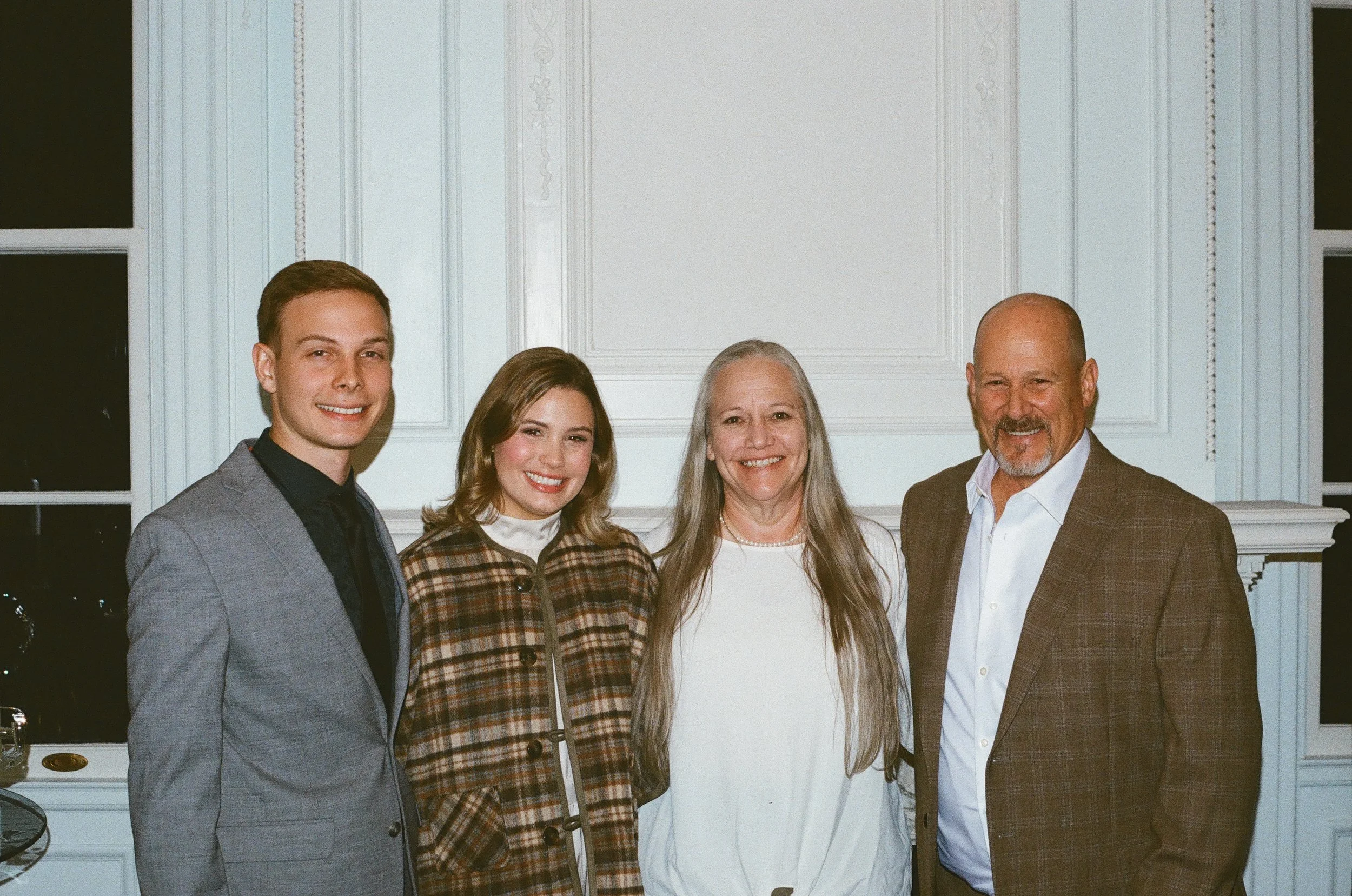 A group of four people standing inside a room with white walls and picture window, smiling at the camera.