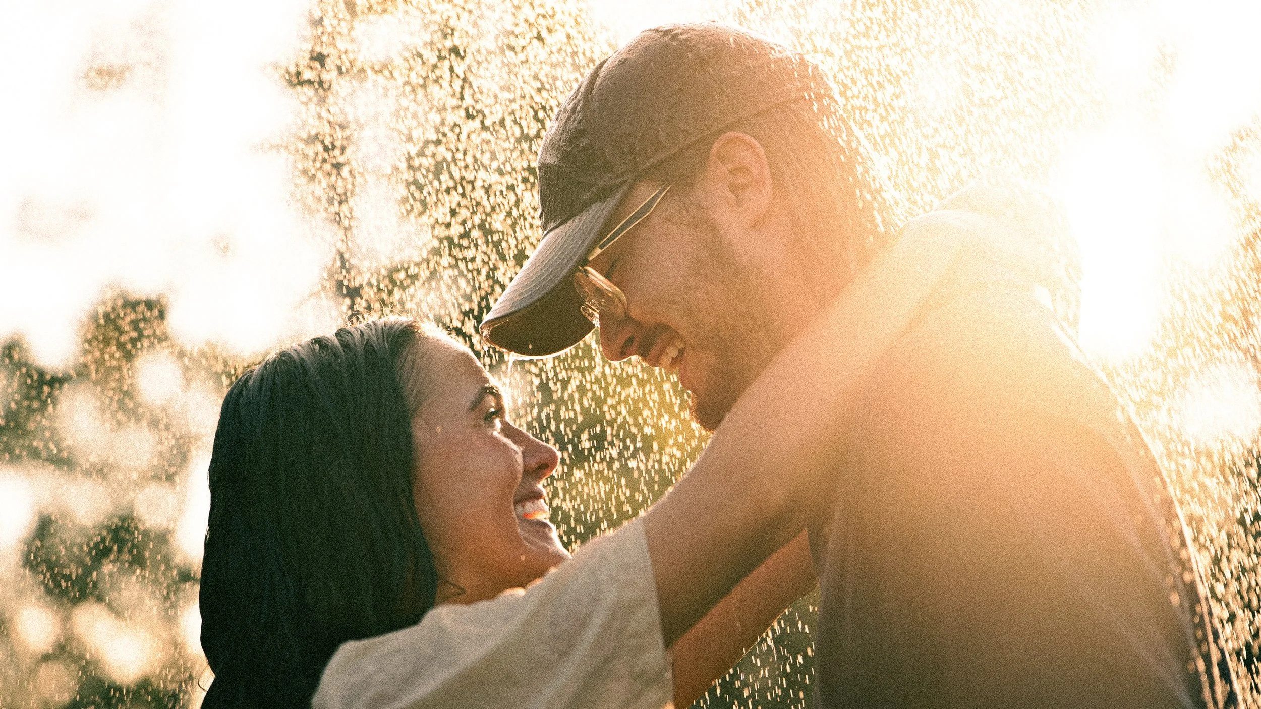 A couple smiling and looking into each other's eyes while standing close together in water during sunset.
