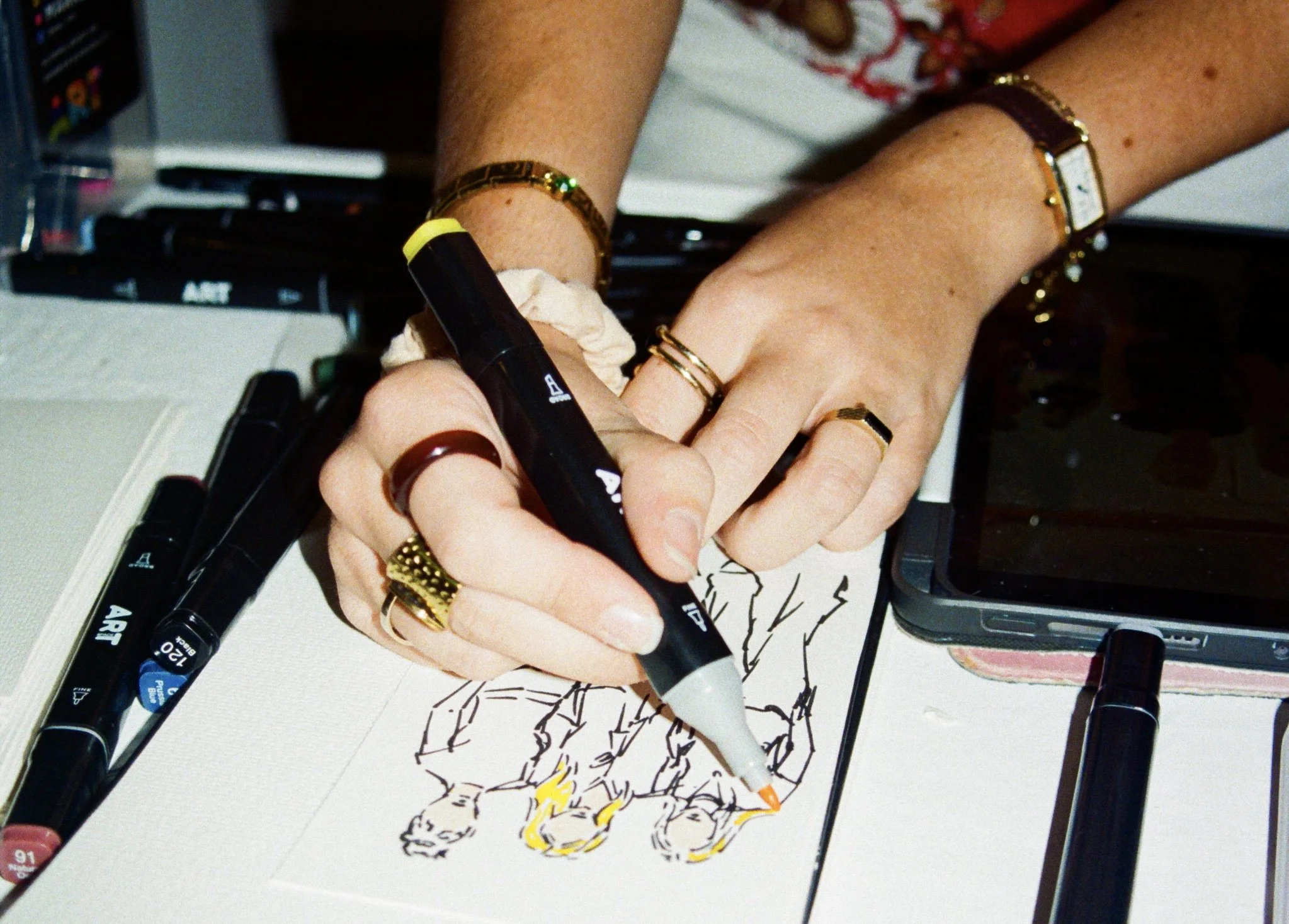 Liberty drawing guests with black markers on white paper, with their hands adorned with rings and bracelets.
