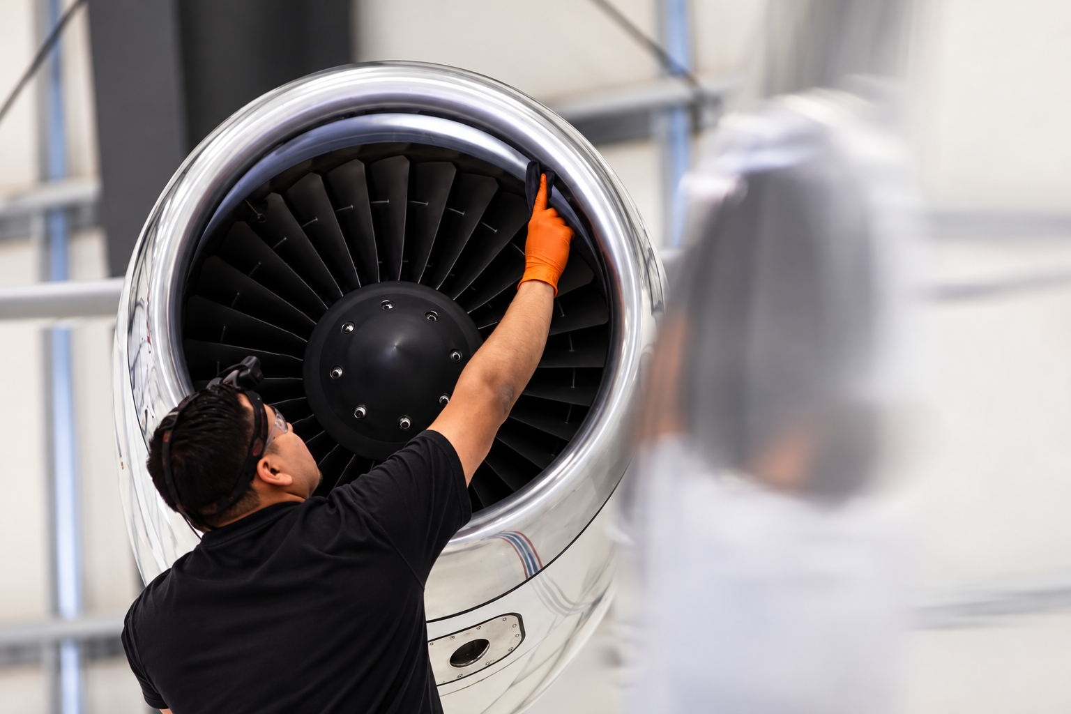 Mitarbeiter mit Schutzbrille und Handschuhen repariert Triebwerkschaufel eines Flugzeugtriebwerks in einer Werkstatt.