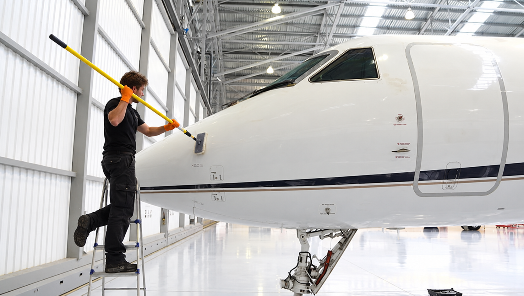Mann reinigt die Nase einer modernen Passagierflugzeug in einem hangarartigen Gebäude.
