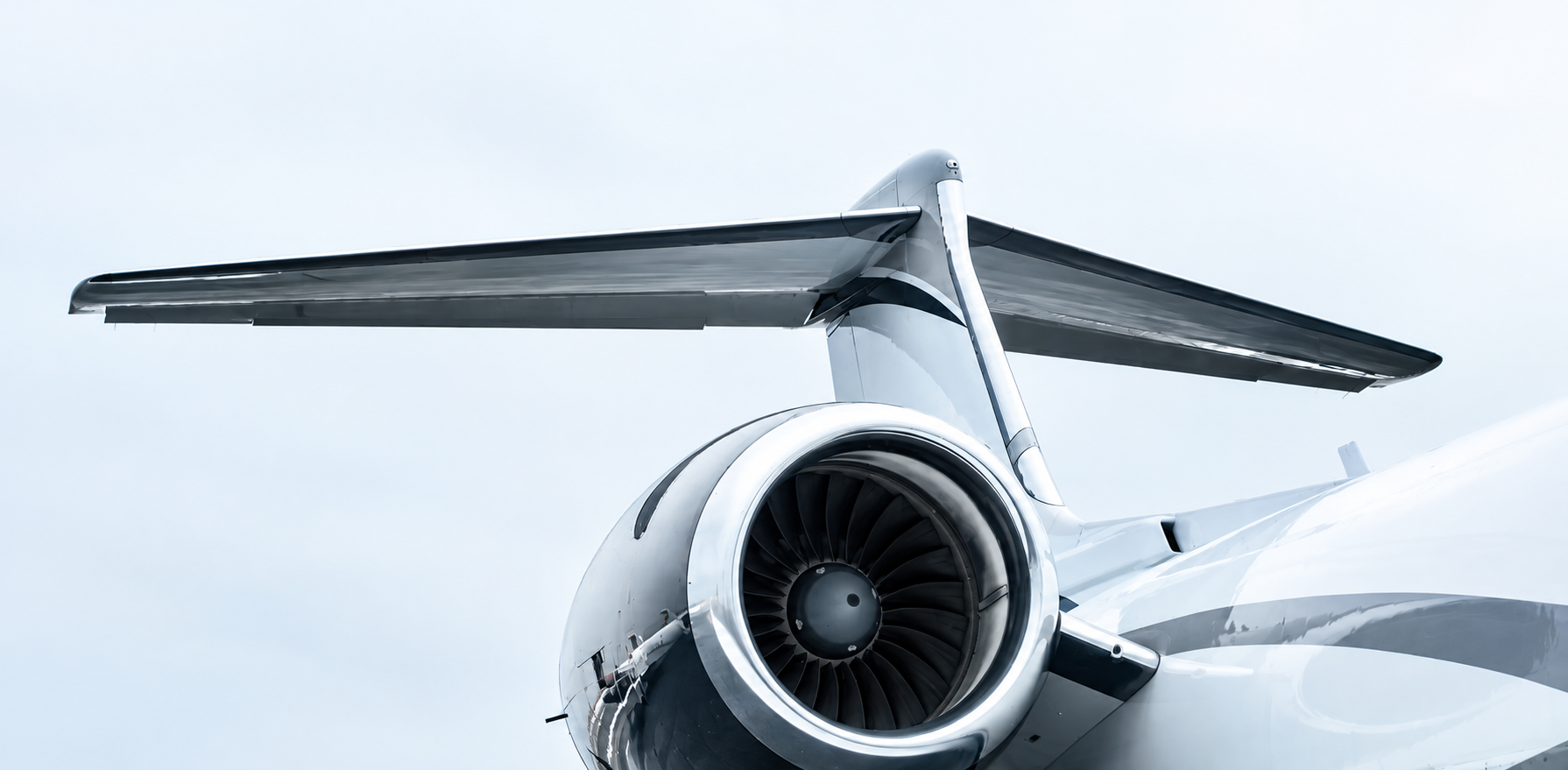 A close-up of the tail section of a modern commercial aircraft, showing the jet engine and horizontal stabilizer against a cloudy sky.