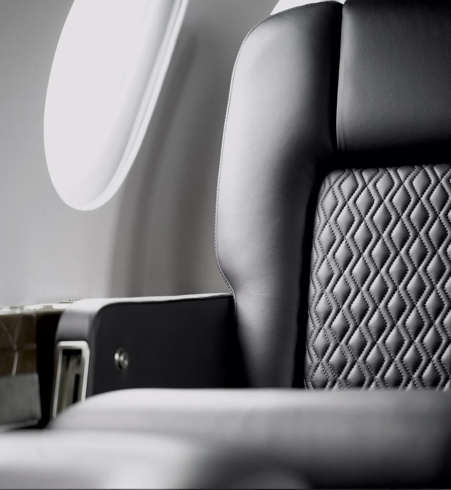 Nahaufnahme eines Flugzeugsitzes mit schwarzem Lederbezug und einer gepolsterten Kopfstütze, neben einem Fenster