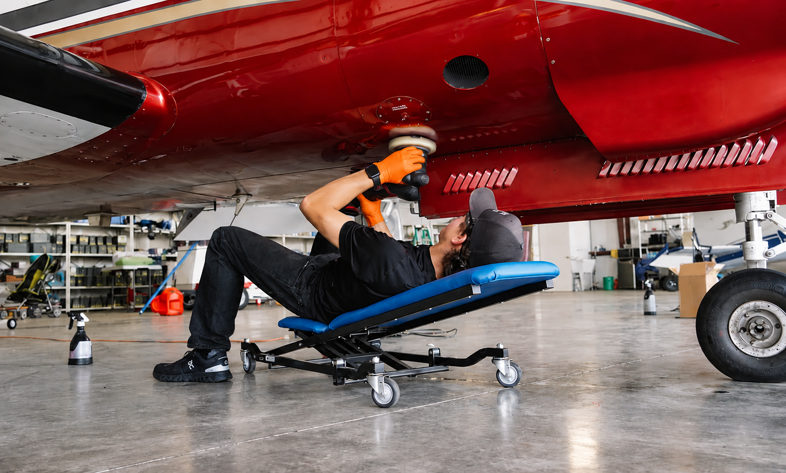 Ein Techniker arbeitet mit einem Poliergerät an der Unterseite eines roten Flugzeugs im Hangar.