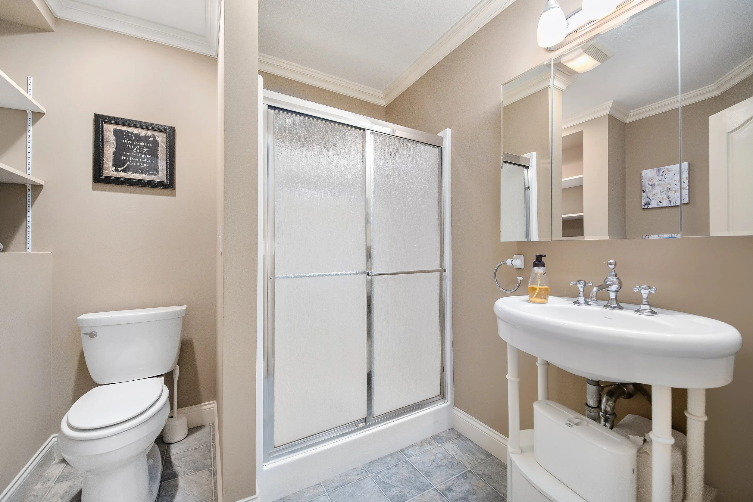 Ocoee River Estate features a small bathroom with a toilet, a shower with glass doors, a pedestal sink, a mirror, and wall-mounted light fixtures.