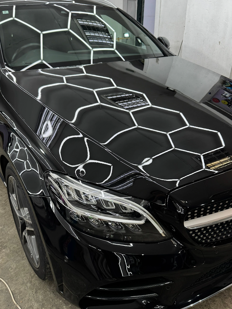 Close-up view of the front of a black luxury car with reflective honeycomb pattern on the hood, parked indoors.
