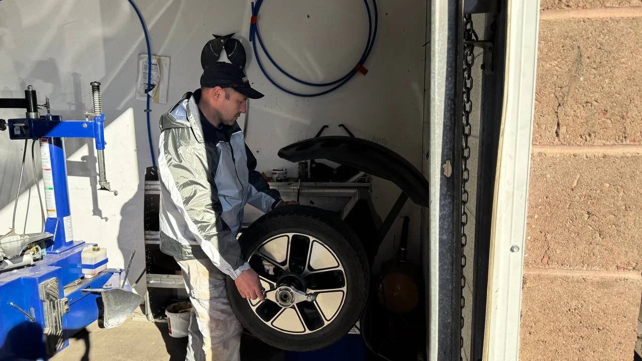 A man working on a tire inside a mobile repair trailer with tools and equipment around him.