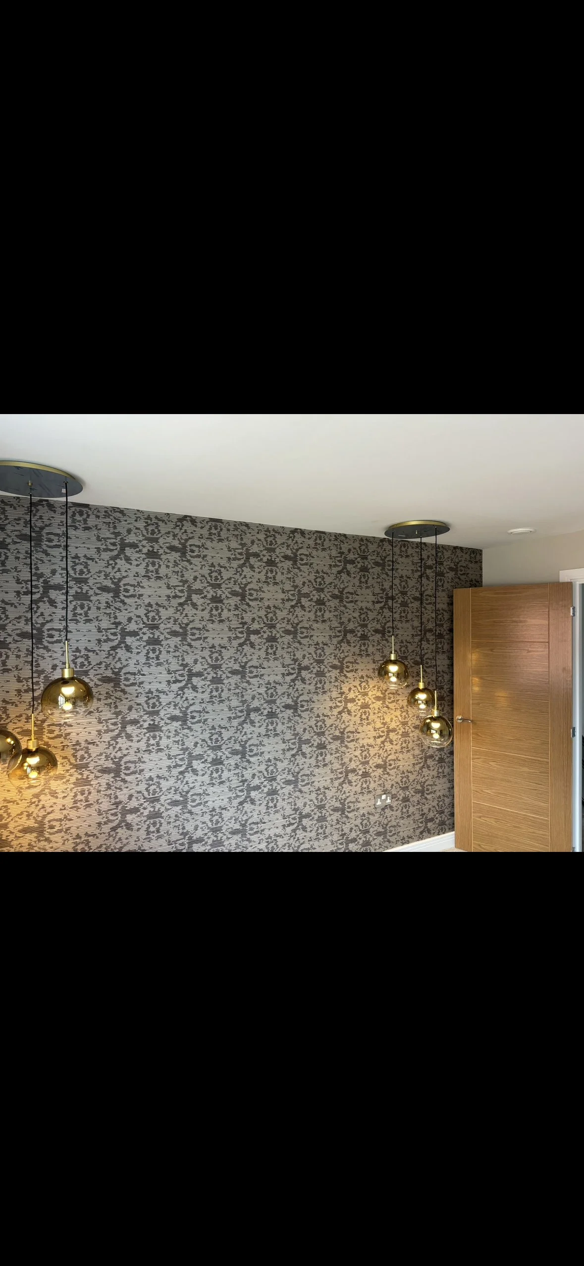 Interior room with patterned wallpaper, hanging gold pendant lights, and a wooden door.