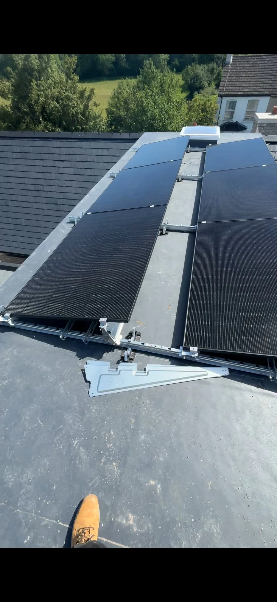 View of solar panels installed on a flat rooftop with a background of trees and neighboring houses.