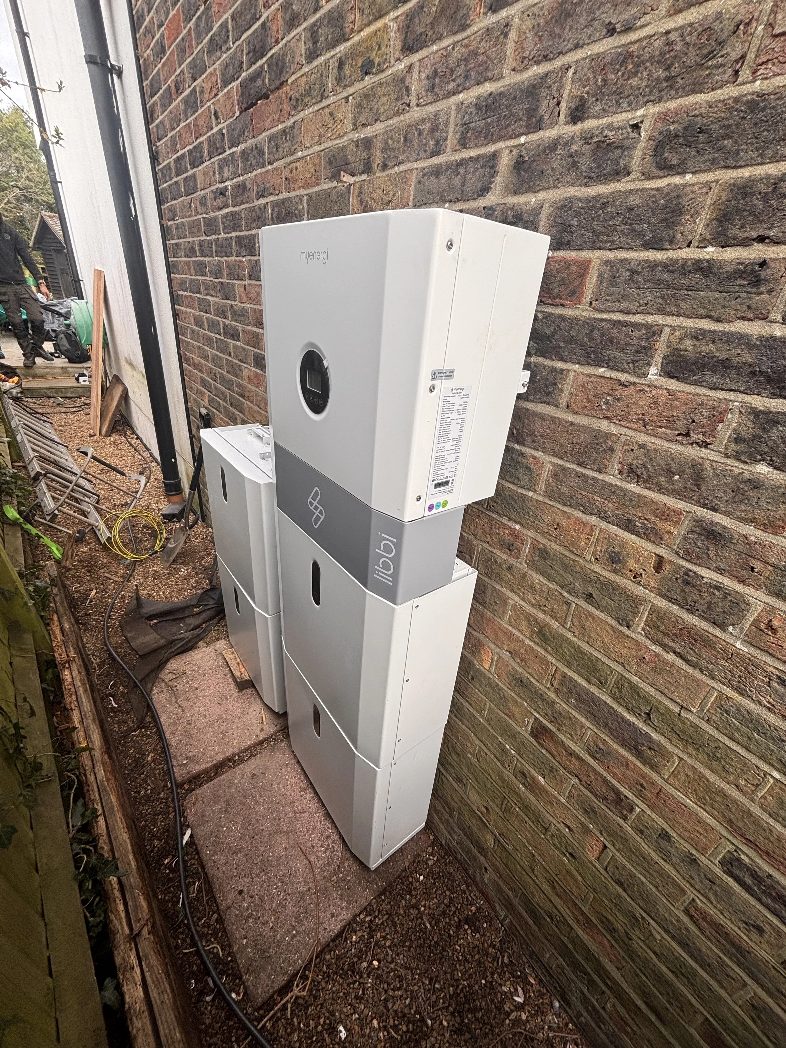 White electric vehicle charging station mounted on a brick wall outside.