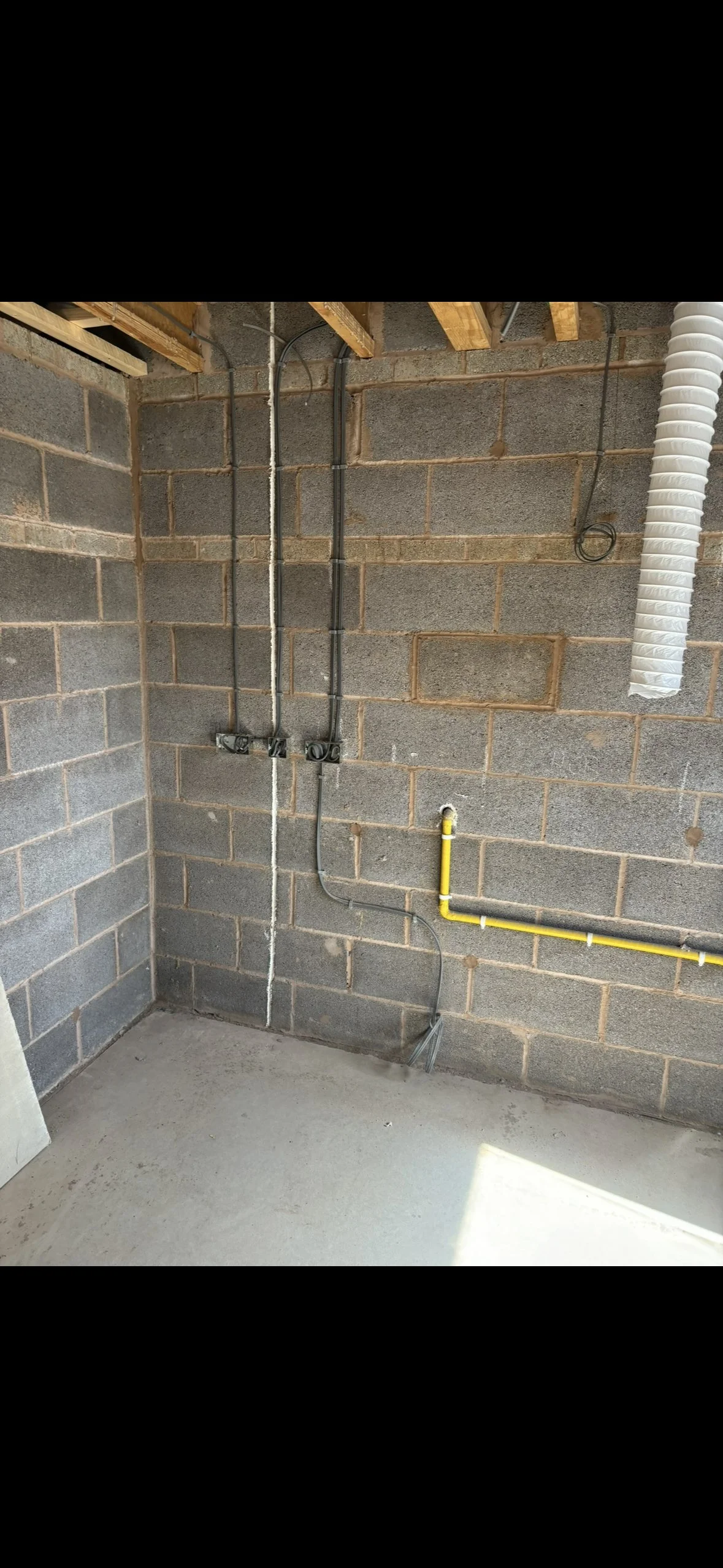 Interior of a construction site showing exposed electrical wiring, outlets, a yellow gas line, and a flexible vent pipe on a cinder block wall.