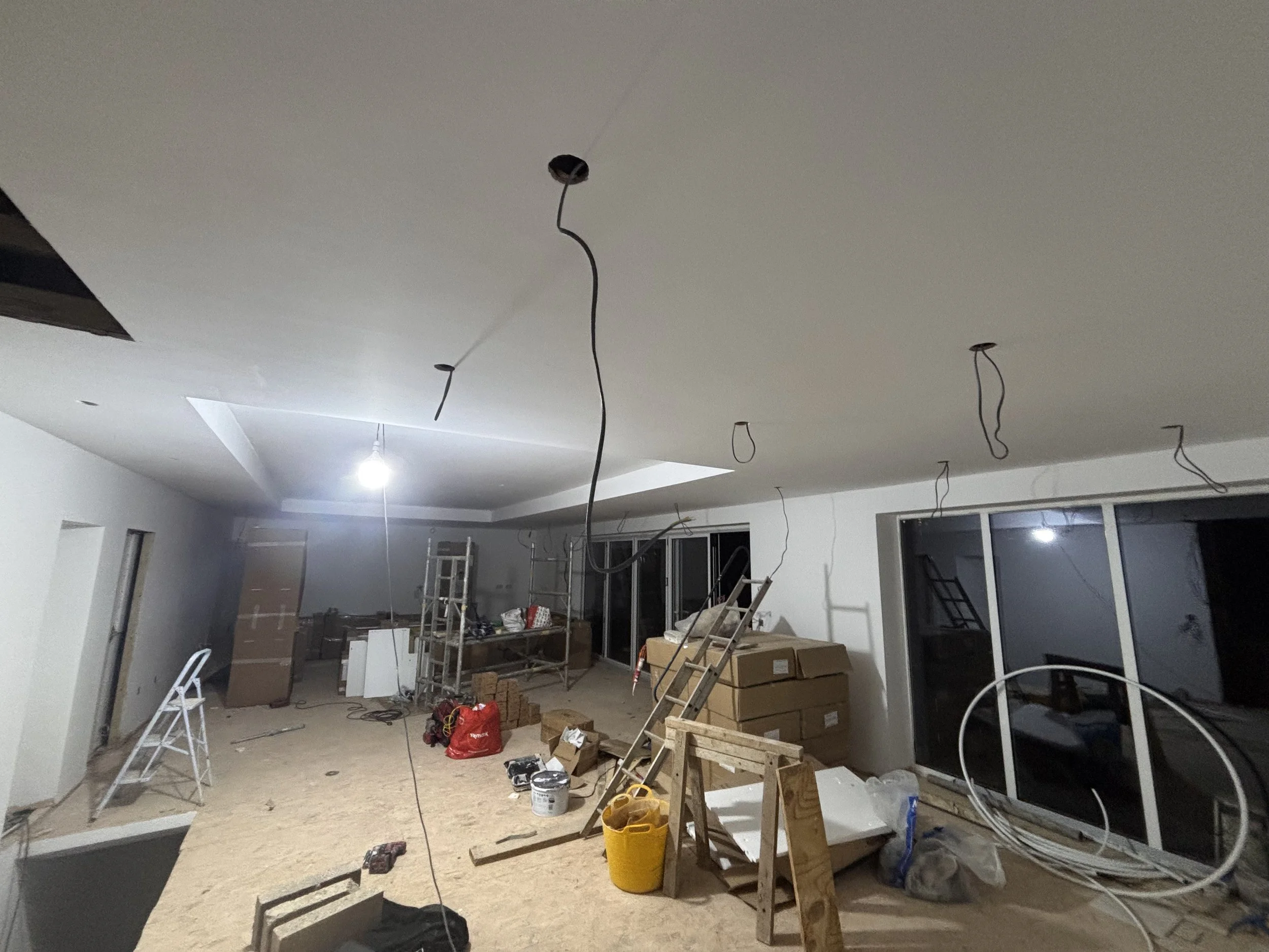 An indoor construction site with unfinished ceiling and scattered construction tools, materials, and ladders