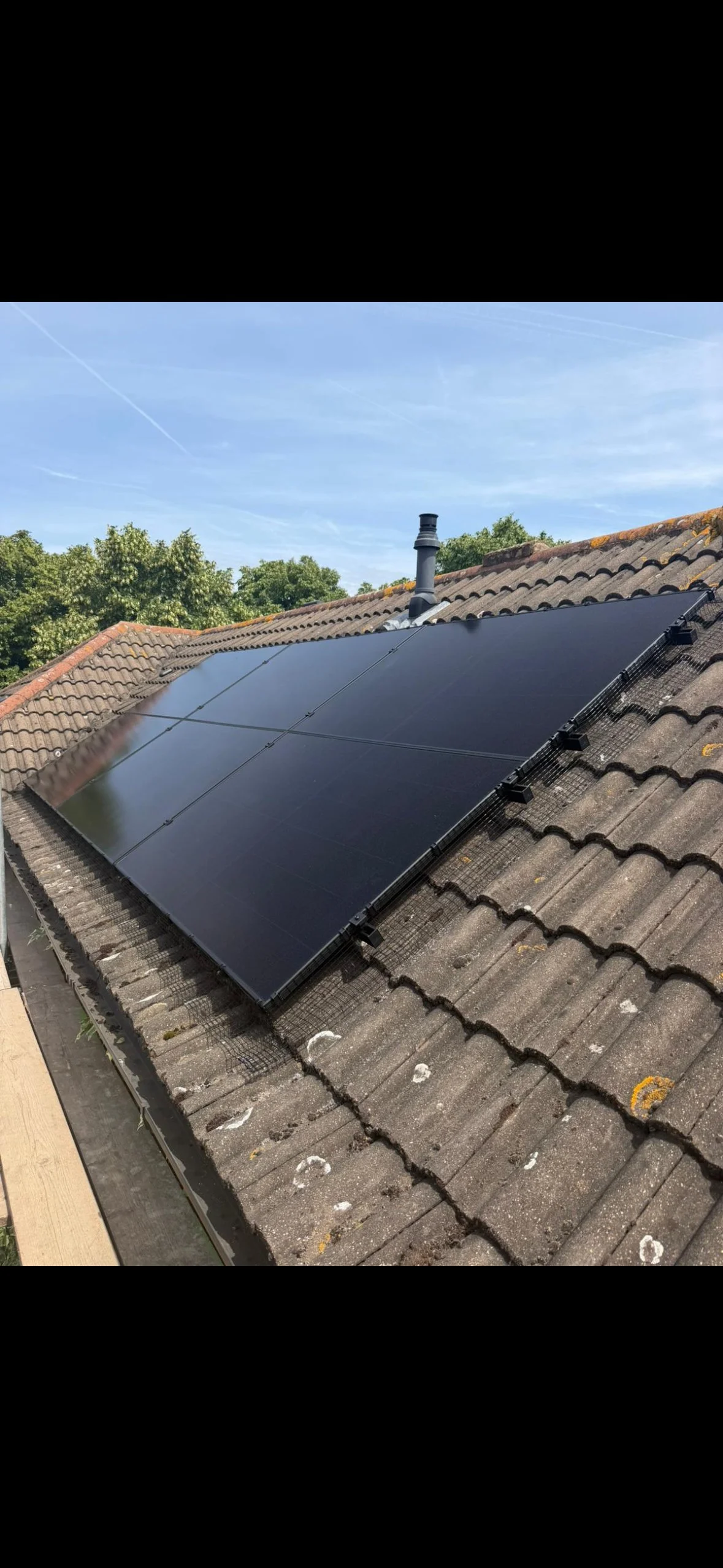 Solar panels installed on the roof of a house with tile roofing, trees in the background, and a chimney on a clear day.