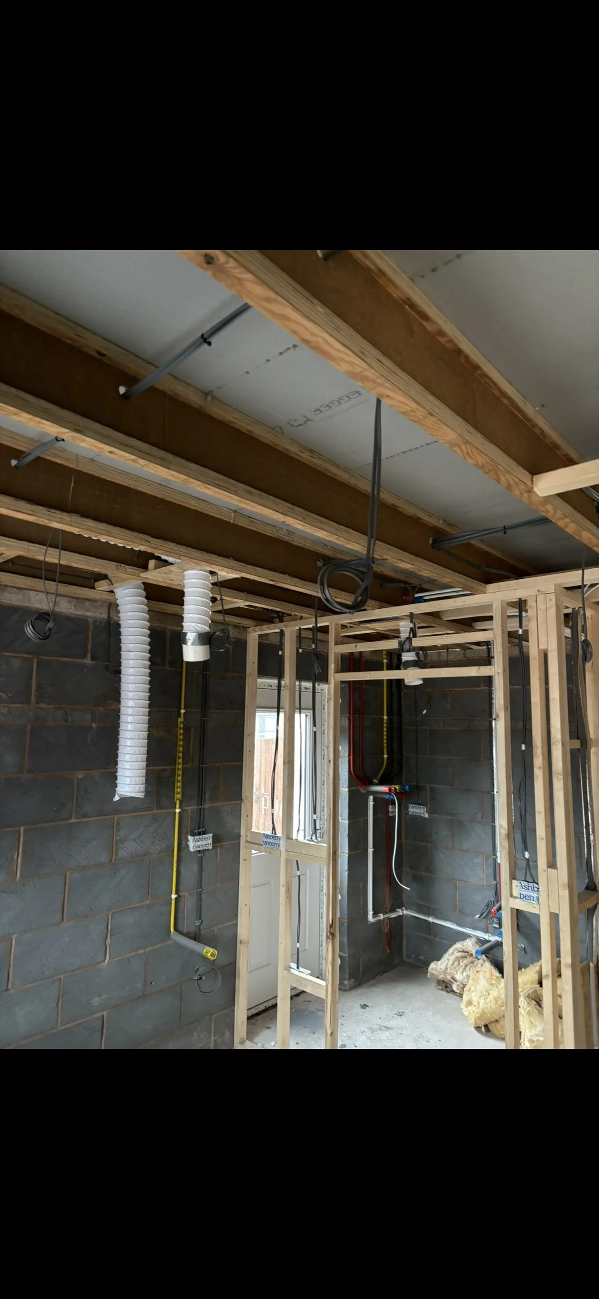 Interior view of a building under construction with exposed framing, electrical wiring, and ventilation ducts.
