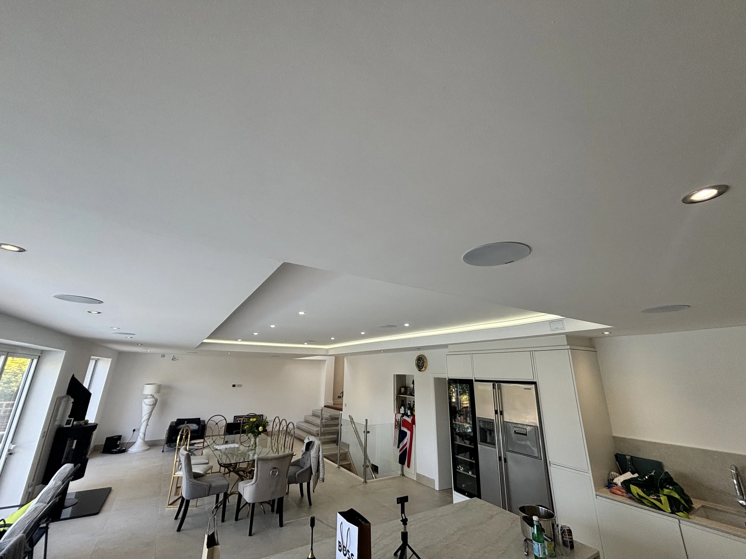 Open-concept living area with a dining table, chairs, and kitchen appliances, ceiling lights, and large windows.