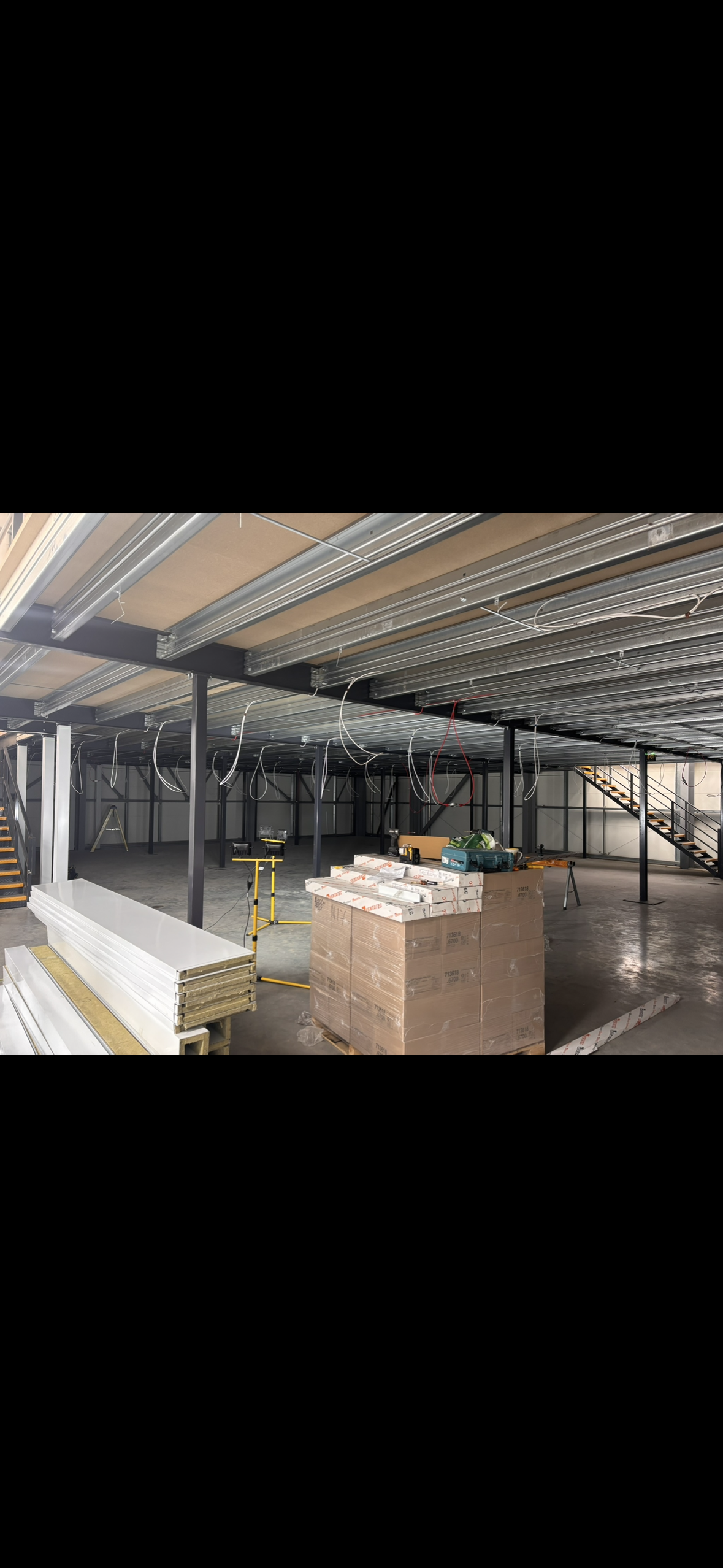 Interior of a building under construction with metal framing, wiring hanging from the ceiling, and building materials and tools on the floor.