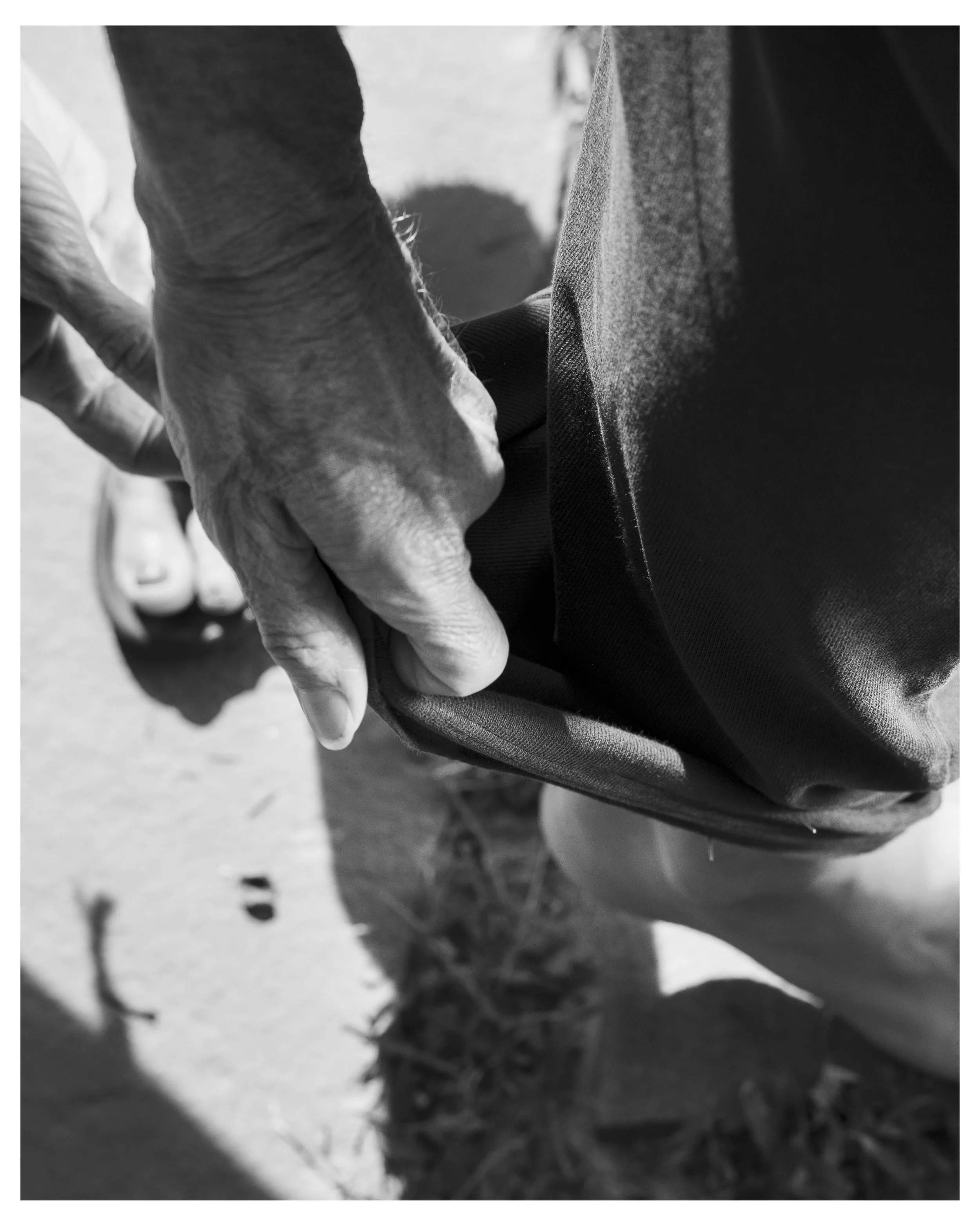 Close-up black and white photo of a person with aged hands stacking a small pile of soil or dirt, possibly while gardening or working outdoors.