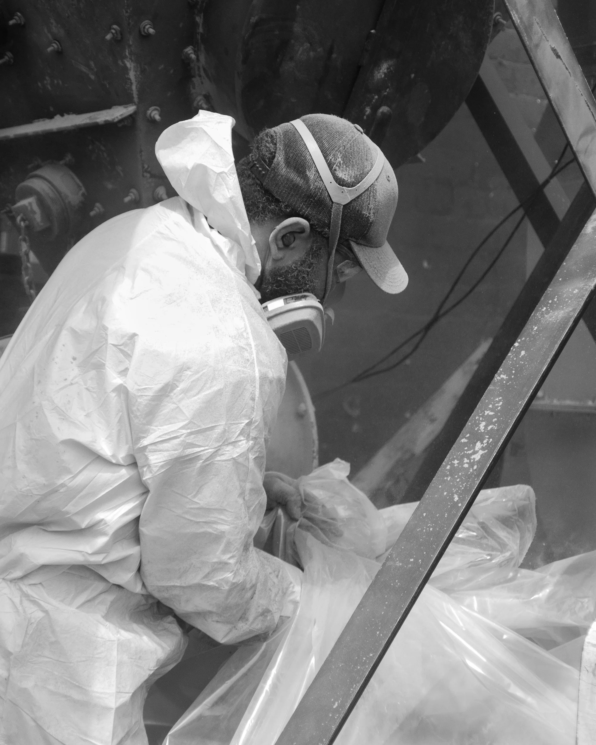 A person wearing safety goggles, a face mask, and protective clothing working on a large machine or industrial equipment.