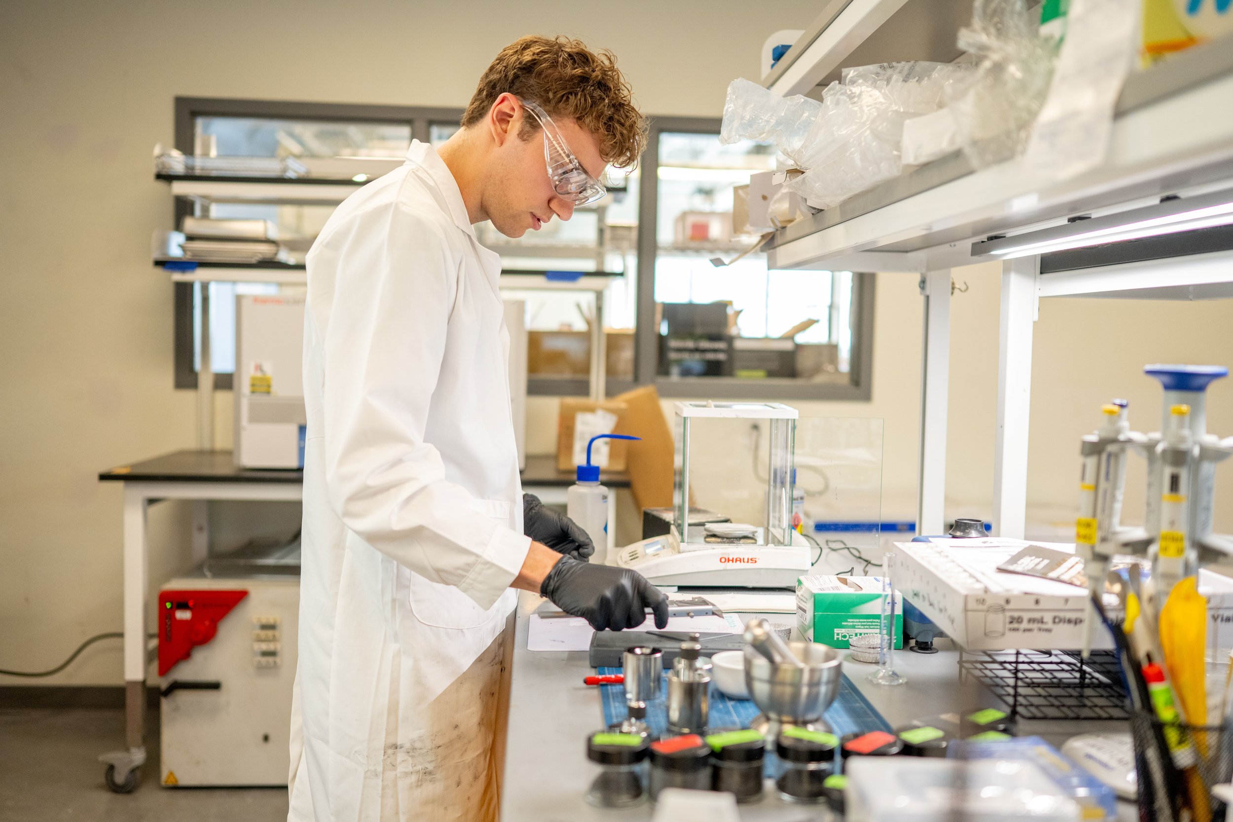 A scientist in a lab coat and safety goggles working with laboratory equipment and chemicals in a modern laboratory.