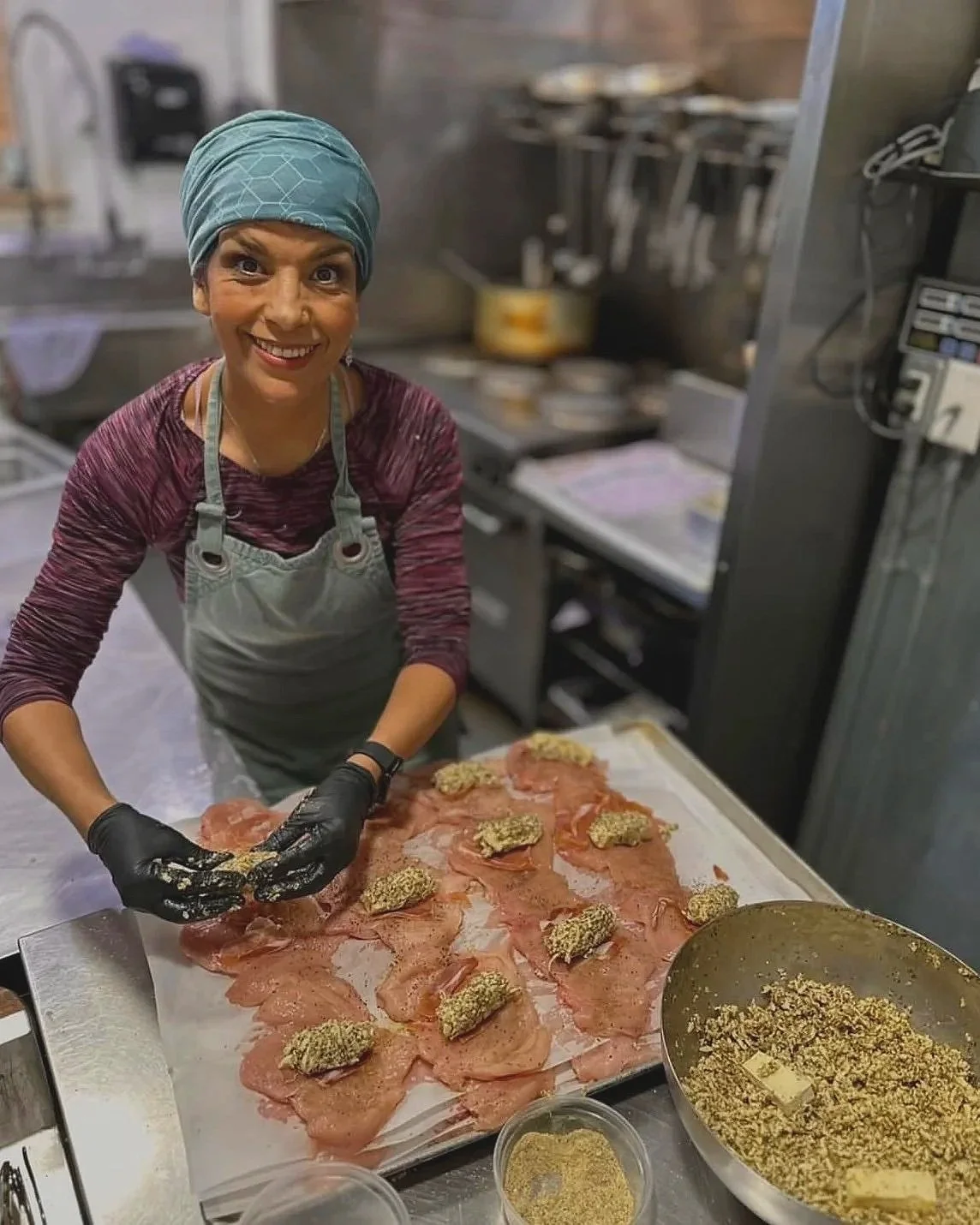 Smiling chef and owner, Bouchra Savard preparing herb-stuffed meat slices in a commercial kitchen