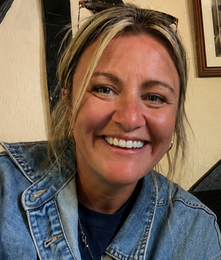 A woman smiling at the camera, wearing a denim jacket and sunglasses on her head.
