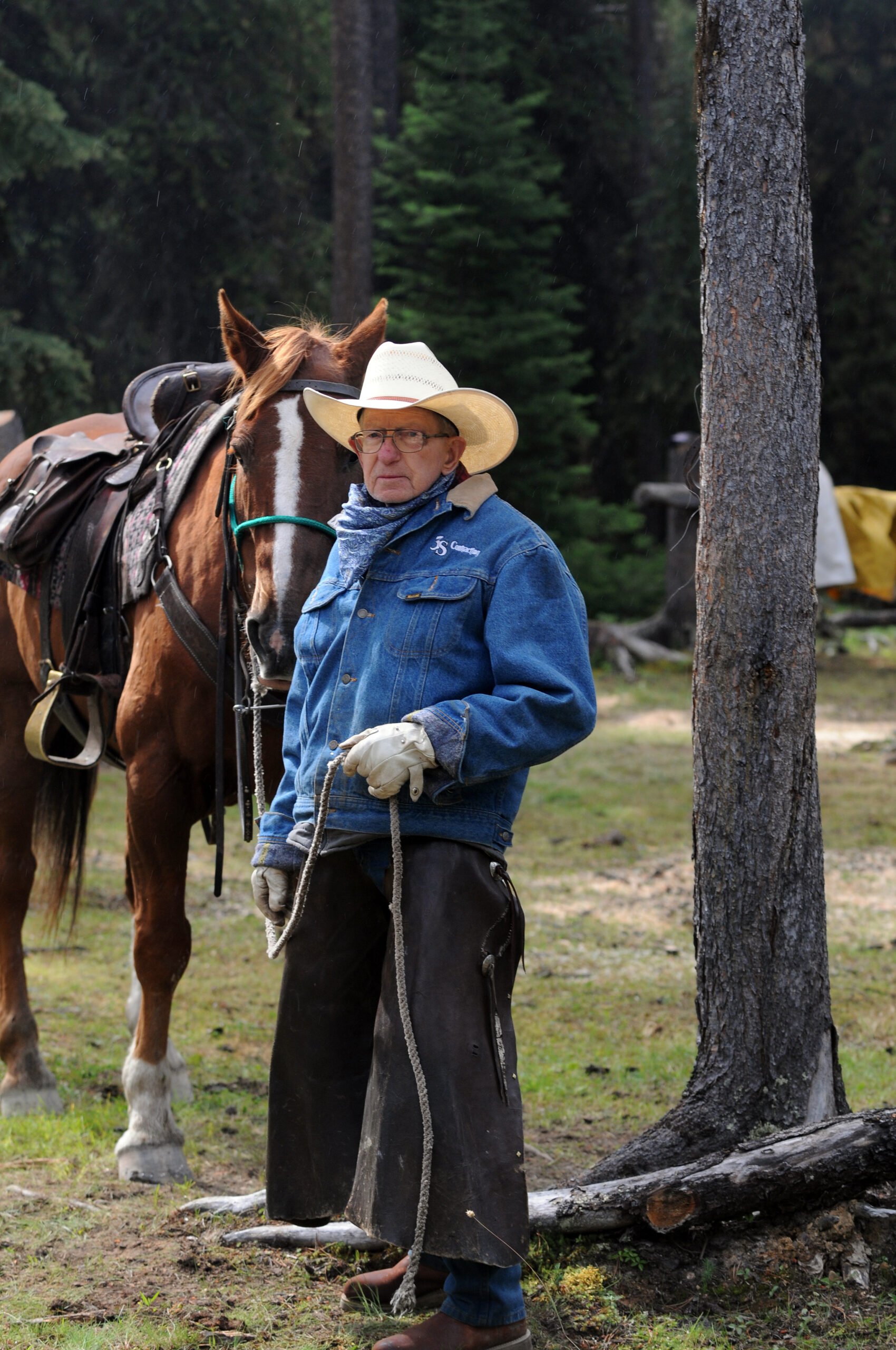 Cowboy standing beside a saddled horse in a rainy forest