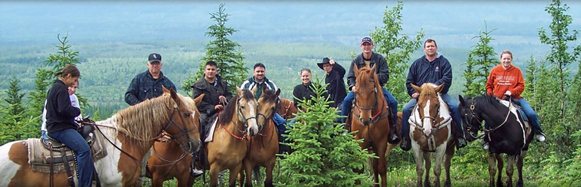 Group of horseback riders posing with horses on a forested mountain overlook