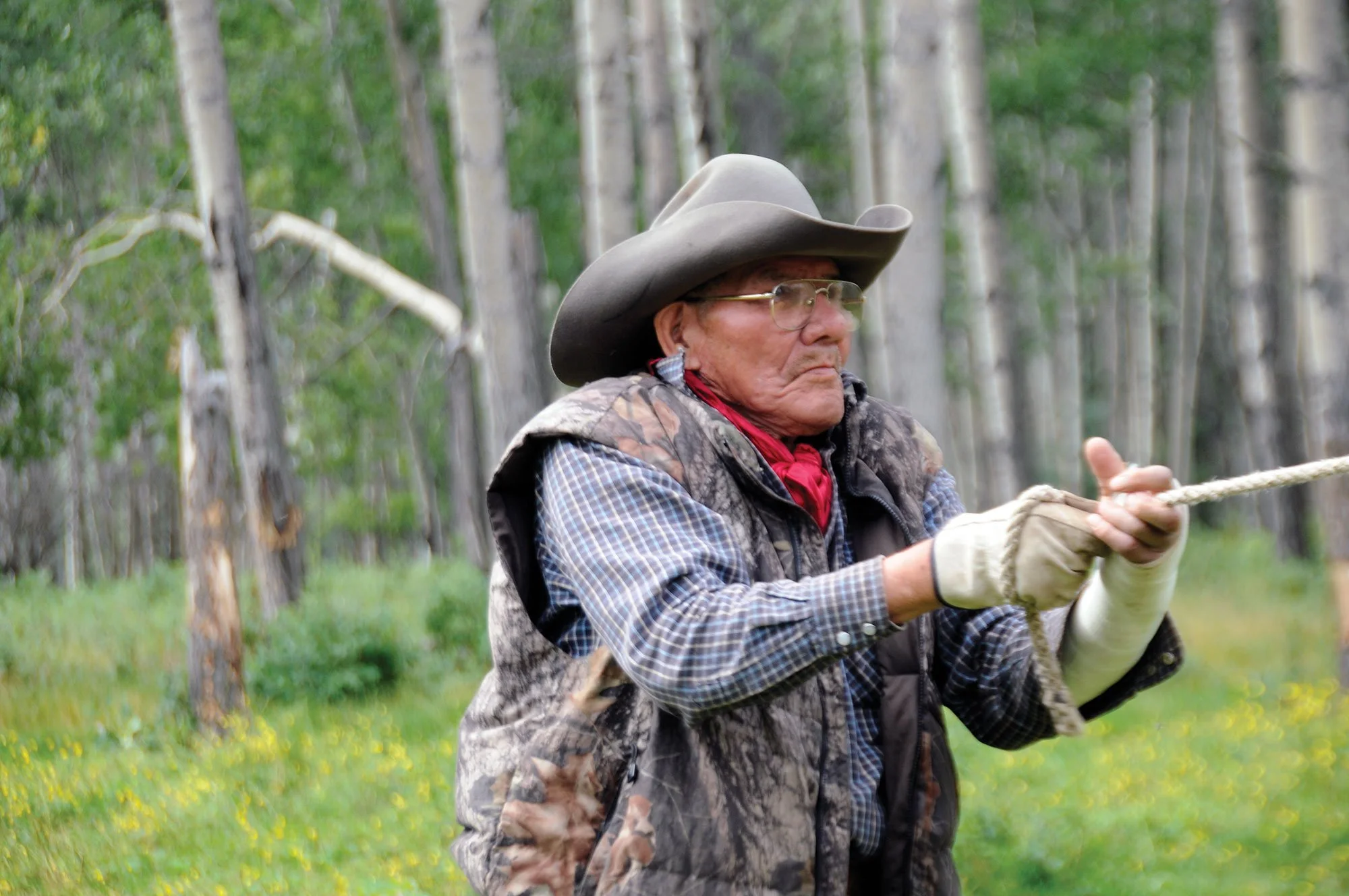 Cowboy in a wide-brimmed hat and camouflage vest pulling a rope in a forest
