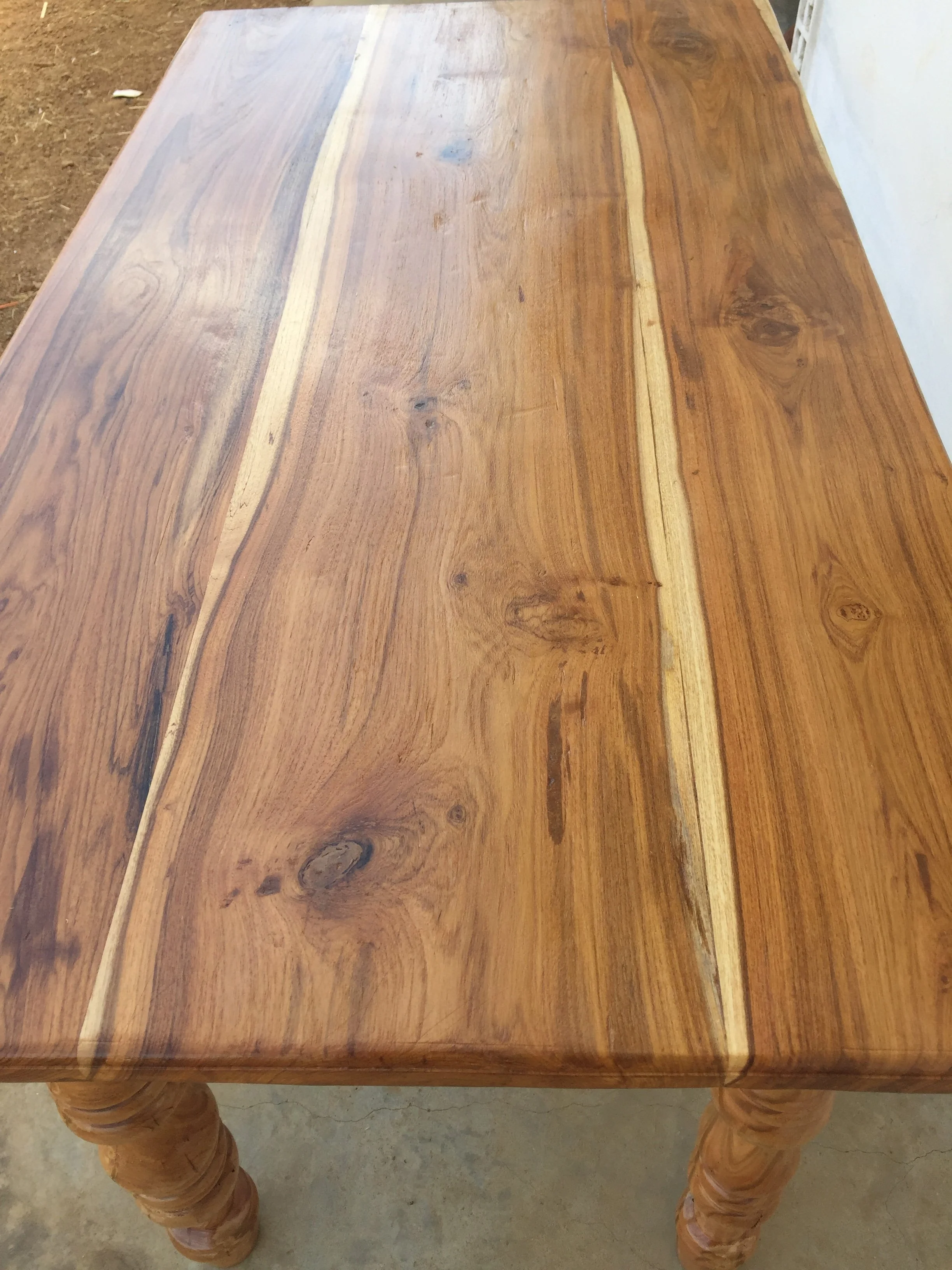 A wooden table with turned legs, showing a natural wood grain finish.