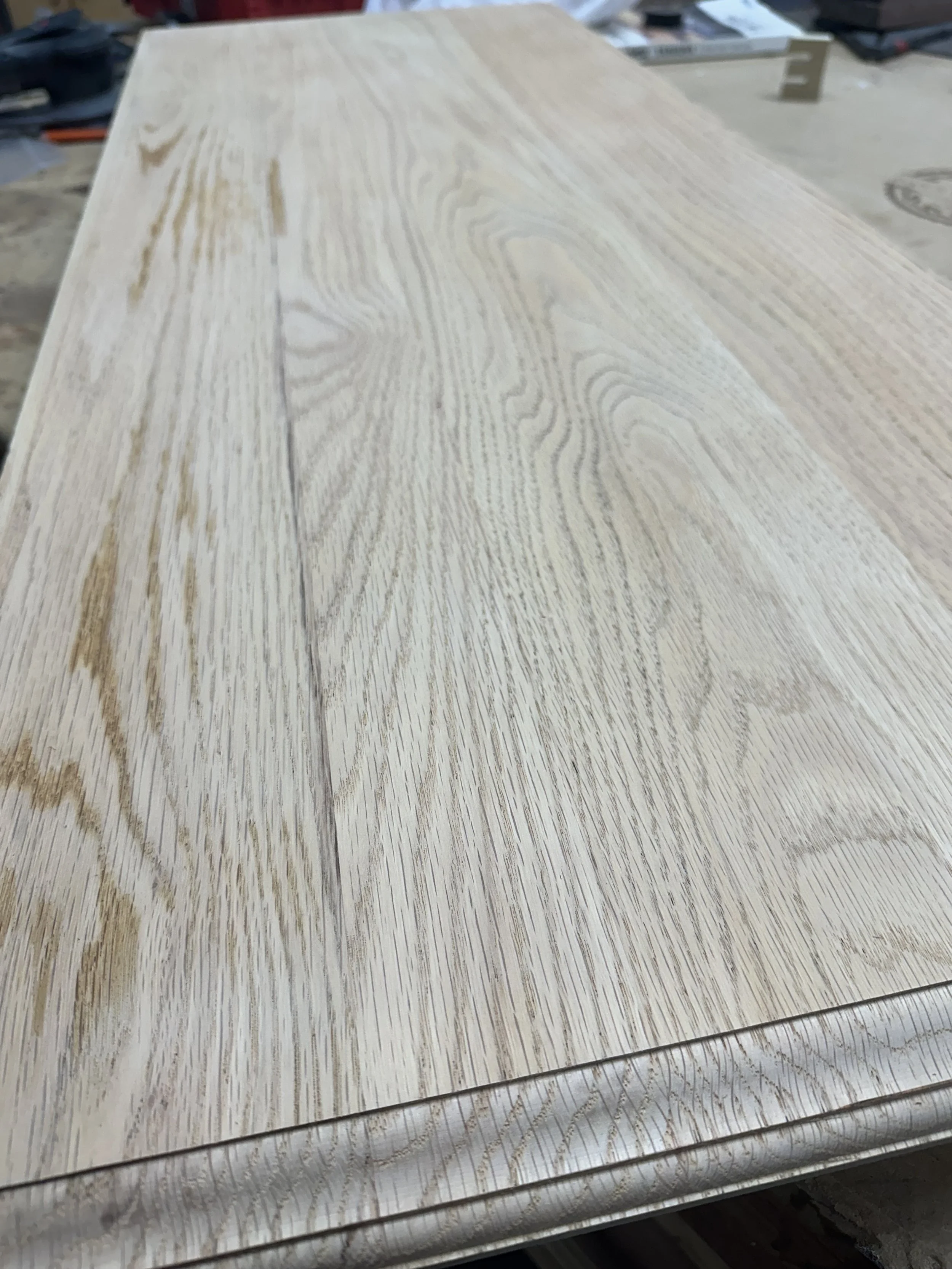 Stack of wooden panels or planks with a light natural wood grain pattern in a workshop setting.