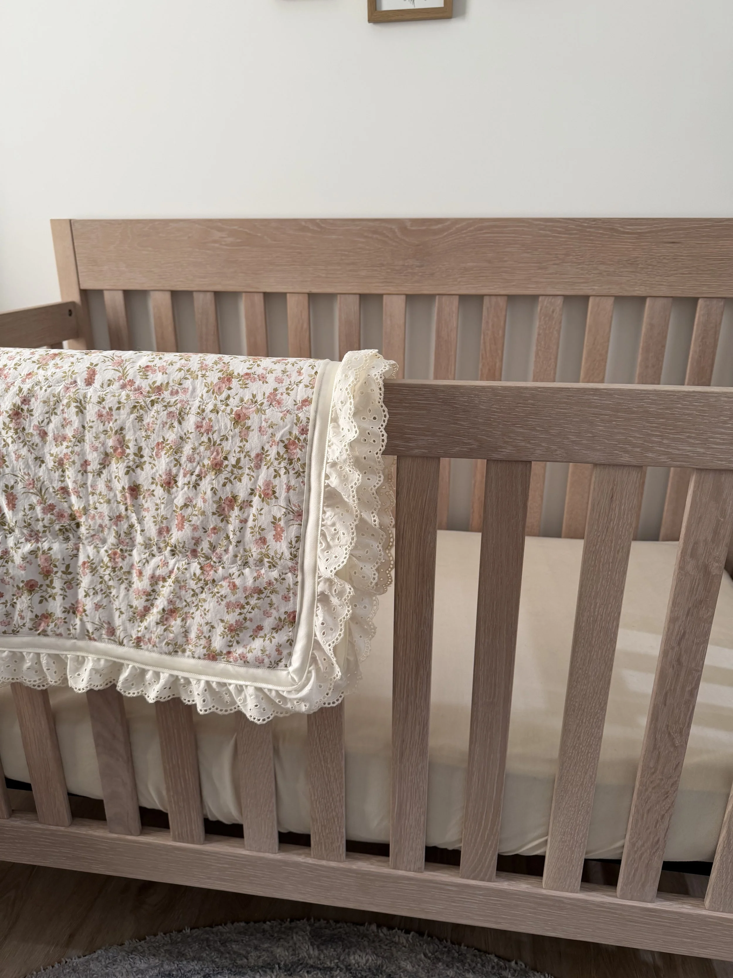 Close-up of a wooden bed frame with a floral-patterned blanket draped over the side.