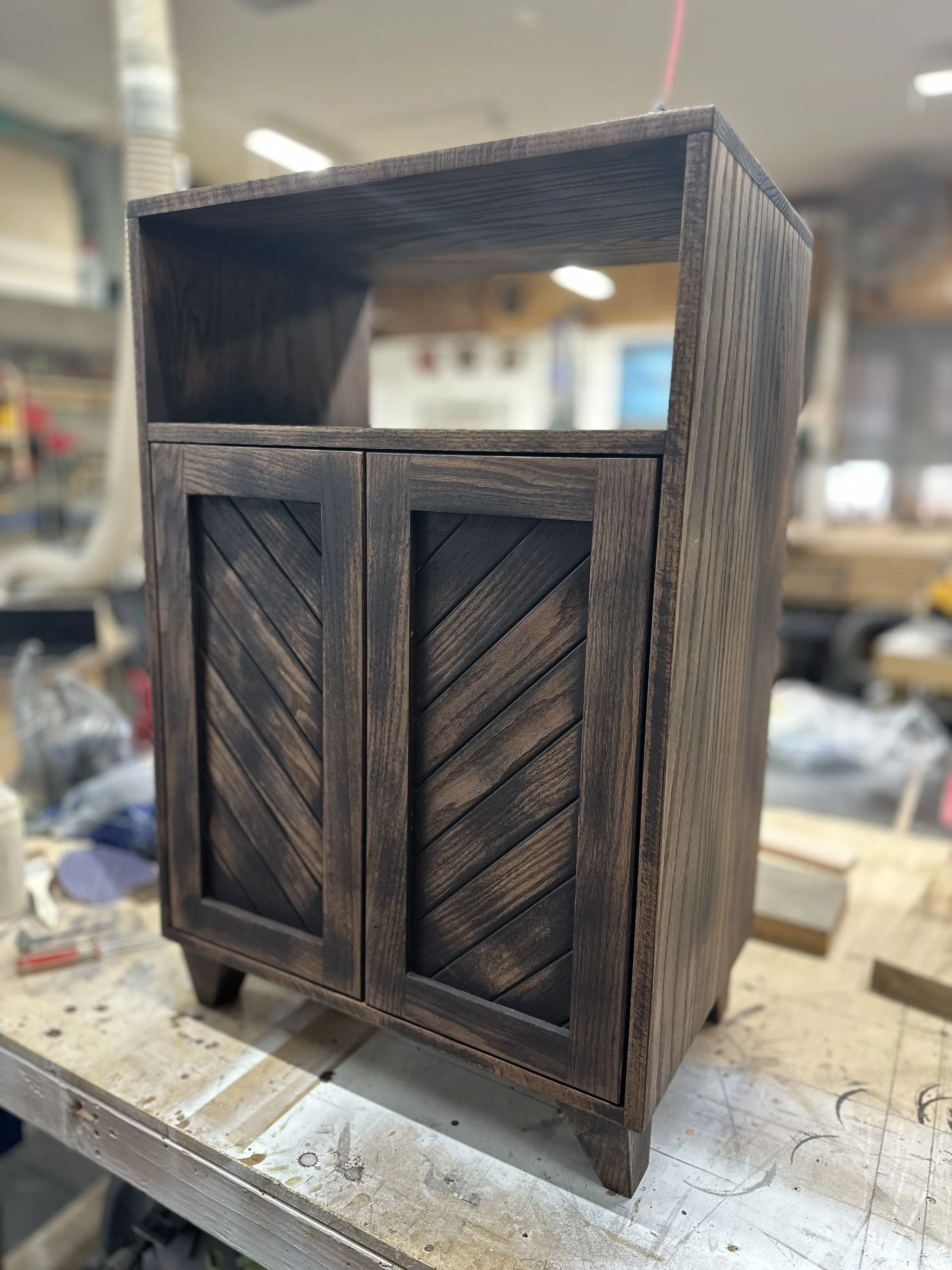 A wooden cabinet with chevron-patterned doors in a woodworking shop.