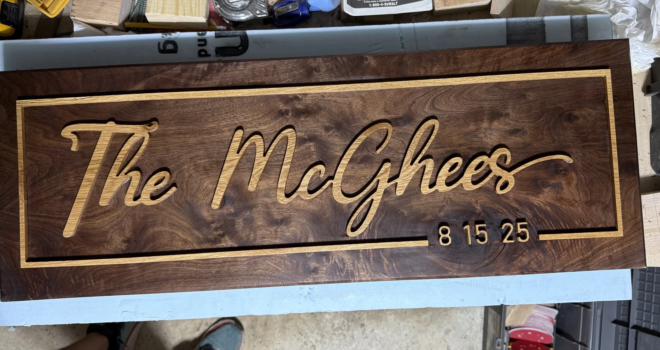 A wooden sign with the words 'The McCyes' carved in script, and date '8 15 25' underneath, accented by a yellow border and engraved details.