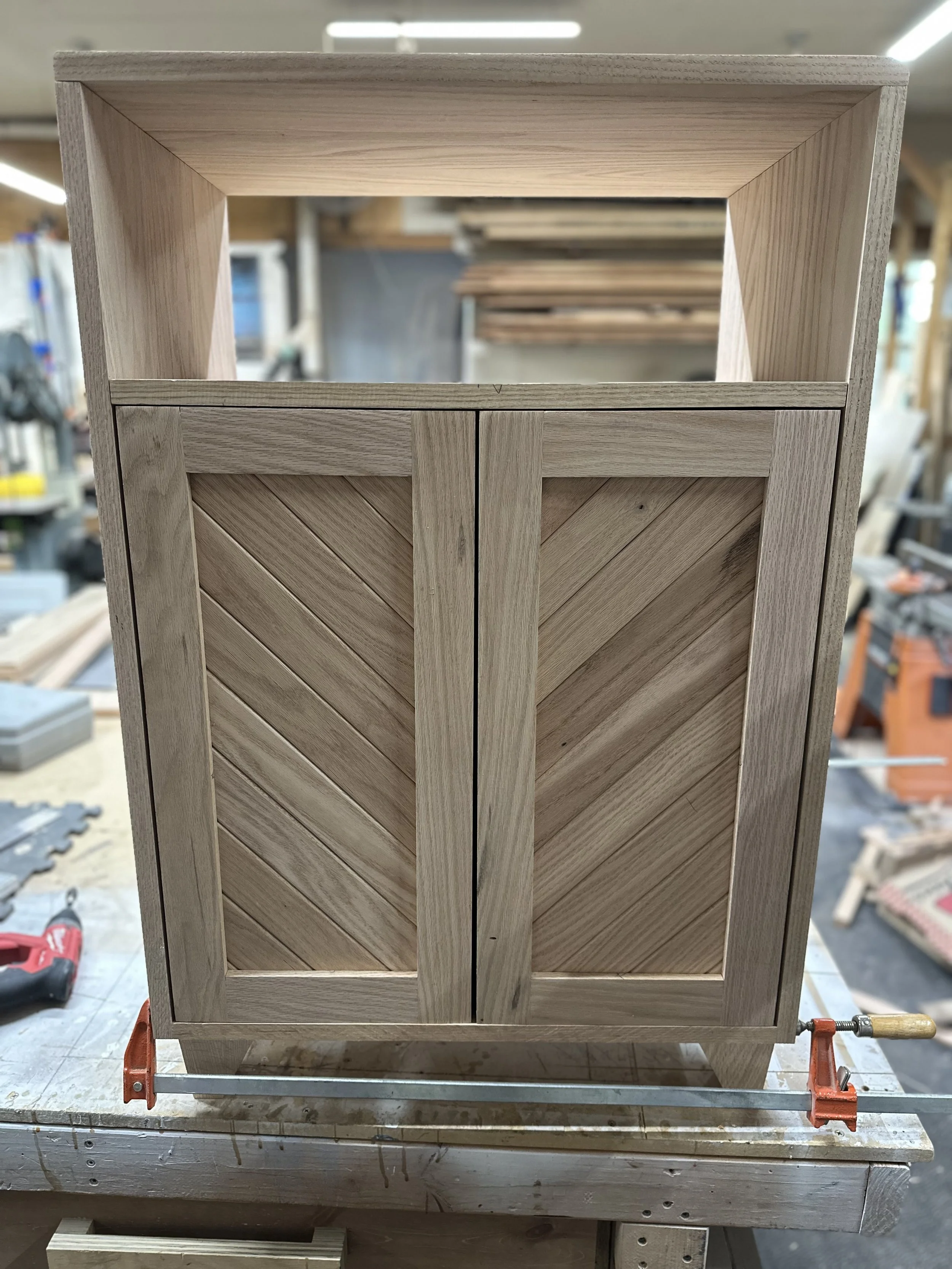 Wooden cabinet with chevron-patterned doors in a woodworking shop.