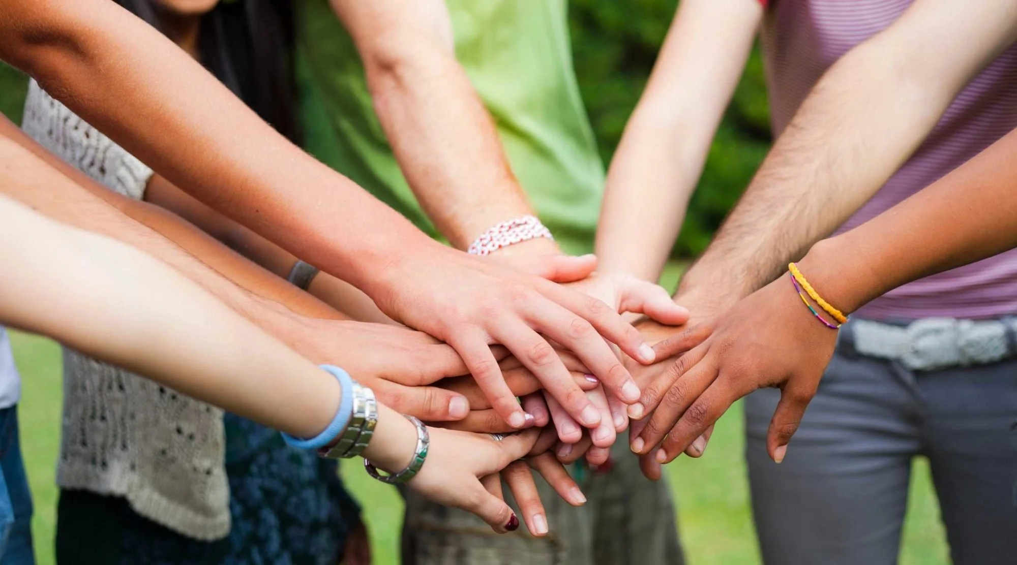 Group of diverse people stacking their hands together outdoors to symbolize teamwork and unity.