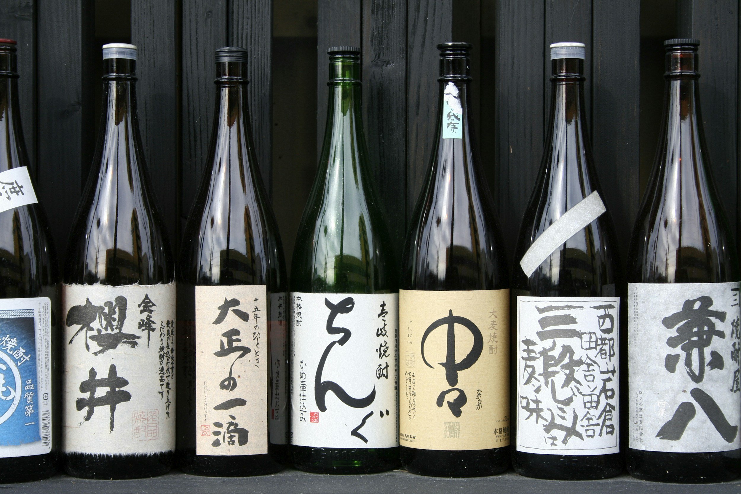 Row of traditional Japanese sake bottles with handwritten Japanese labels on a dark wooden surface.
