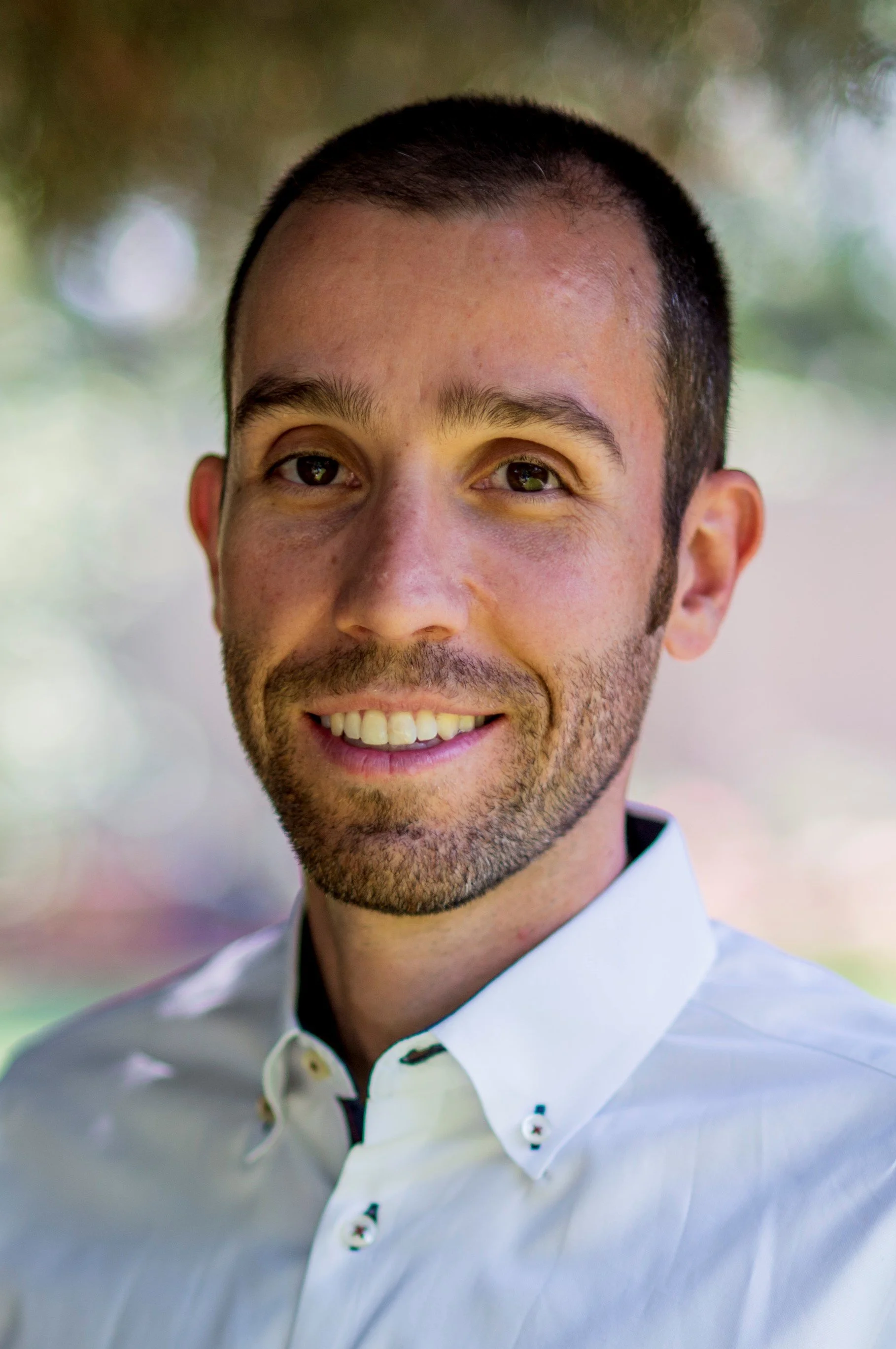 Smiling bearded man in a white dress shirt posing for a portrait.