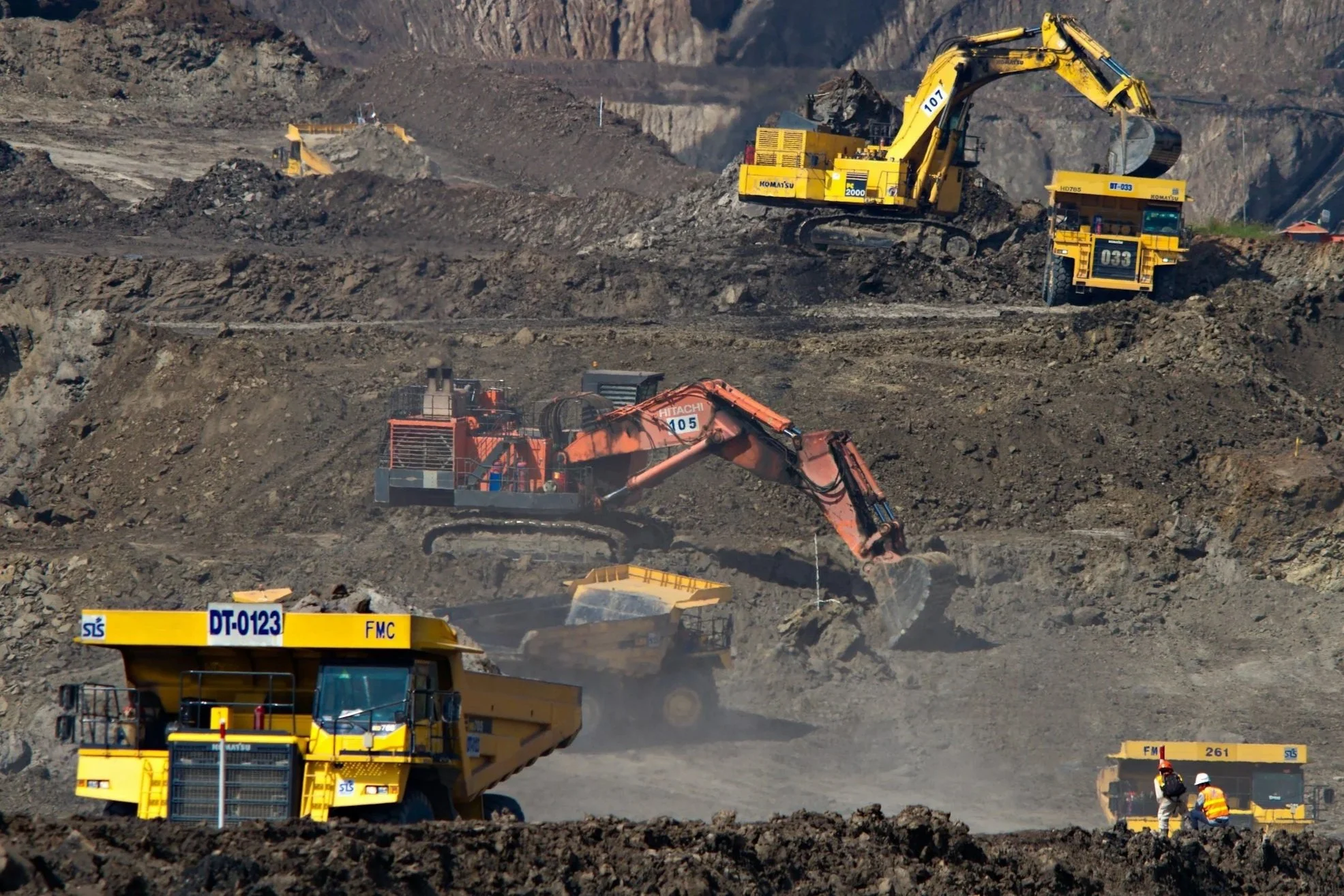 Heavy mining machinery, including excavators and haul trucks, operating in an open-pit mine.