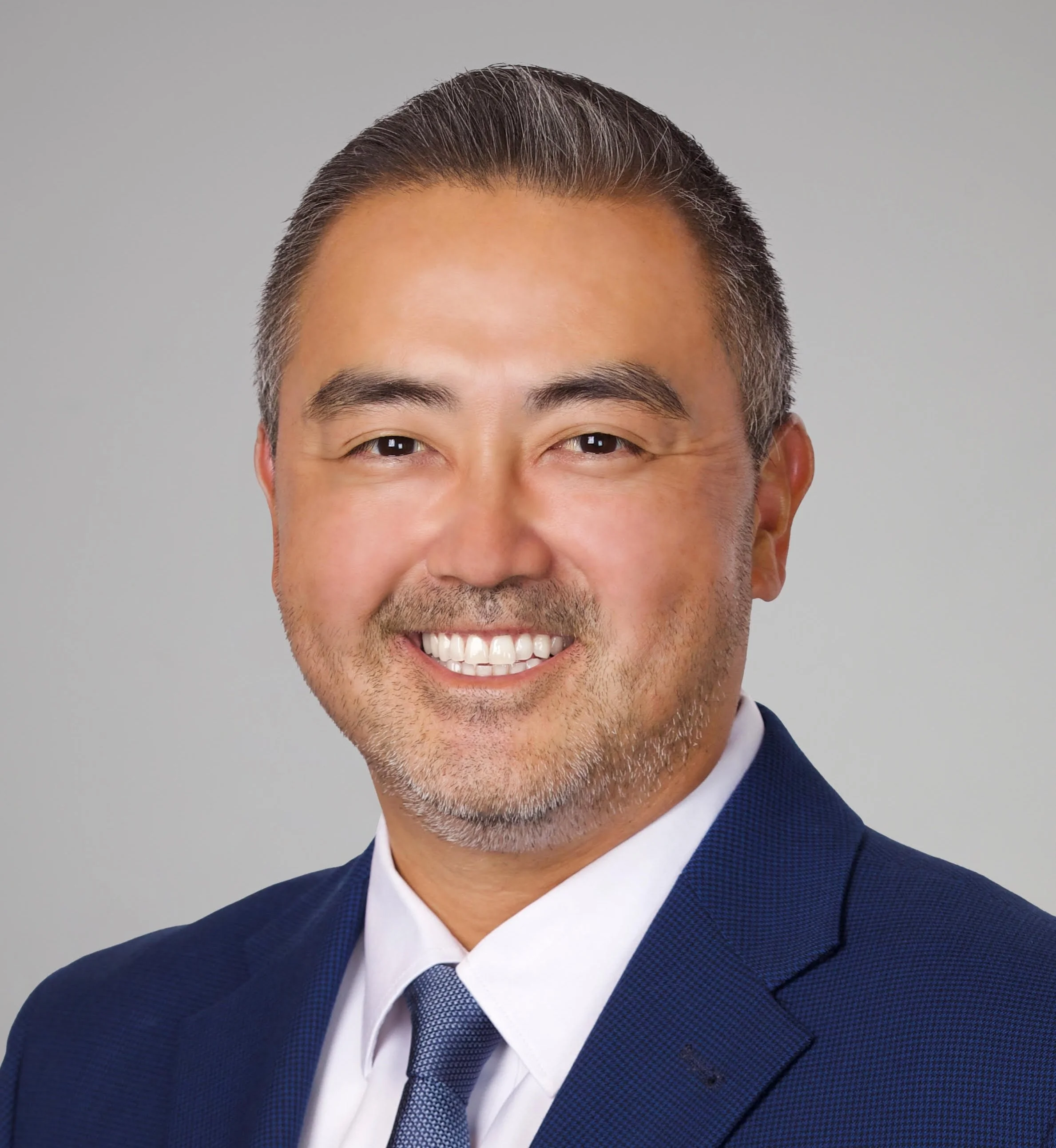 Smiling professional man in a navy suit and tie against a gray background