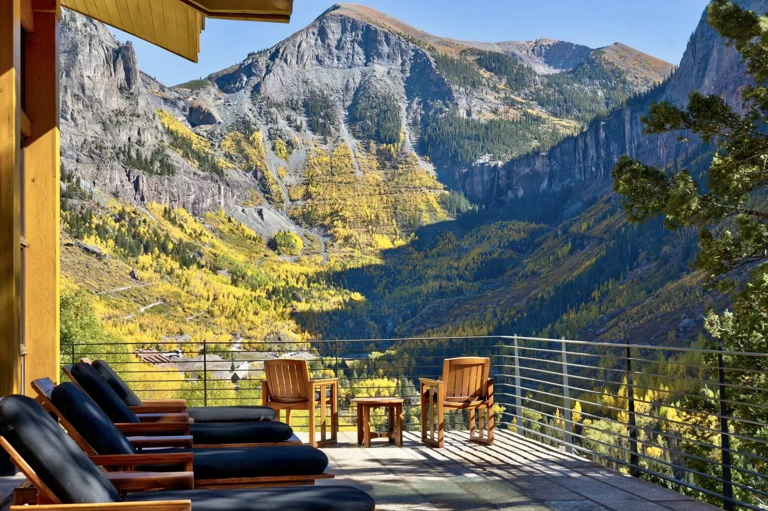 A balcony with chairs overlooking a mountain valley with trees displaying fall colors.
