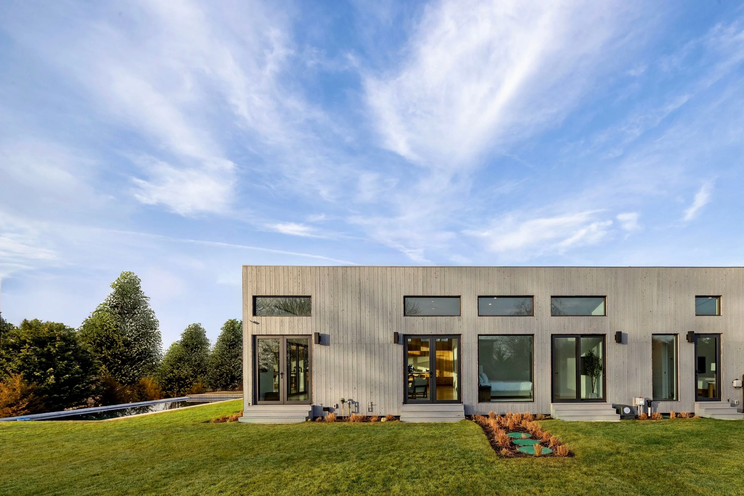 Modern house with large windows and a landscaped yard under a partly cloudy sky.