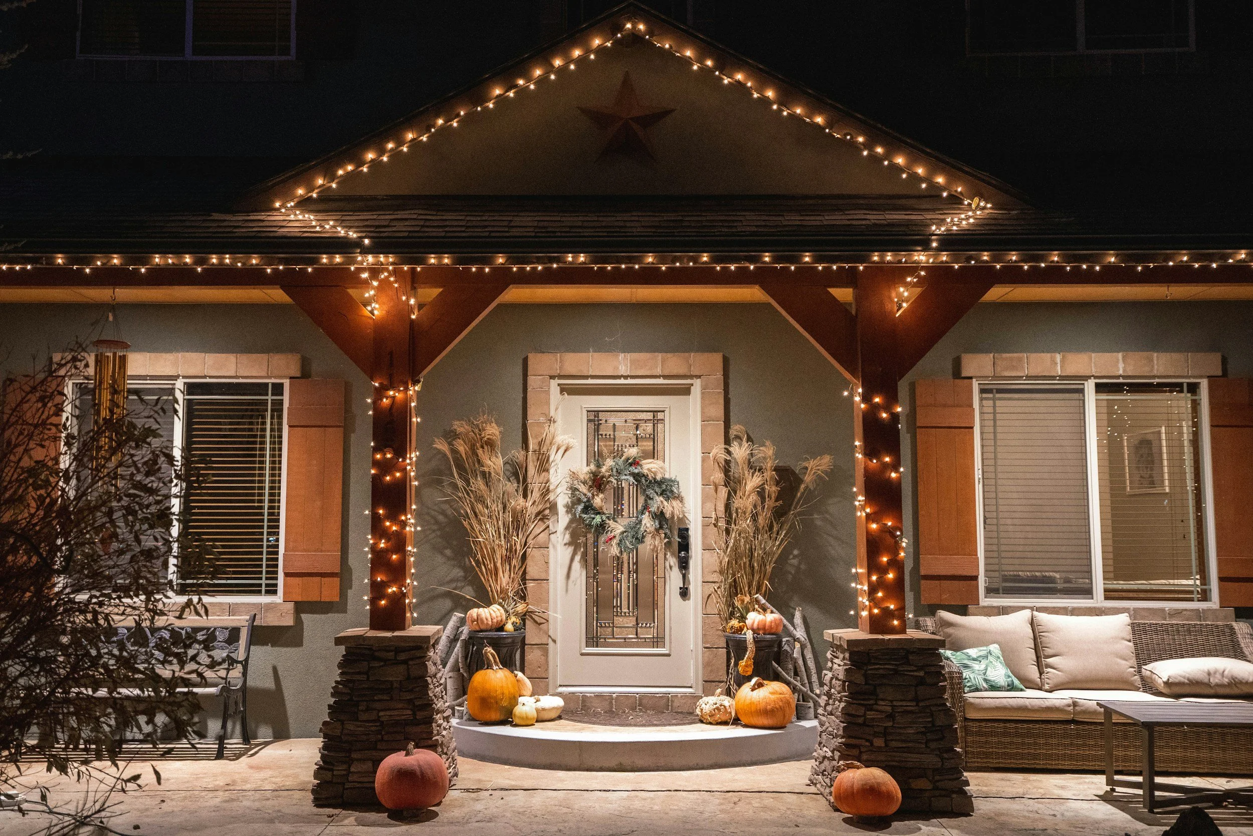 Front porch of a house decorated with string lights, fall pumpkins, and autumn decor, nighttime setting.