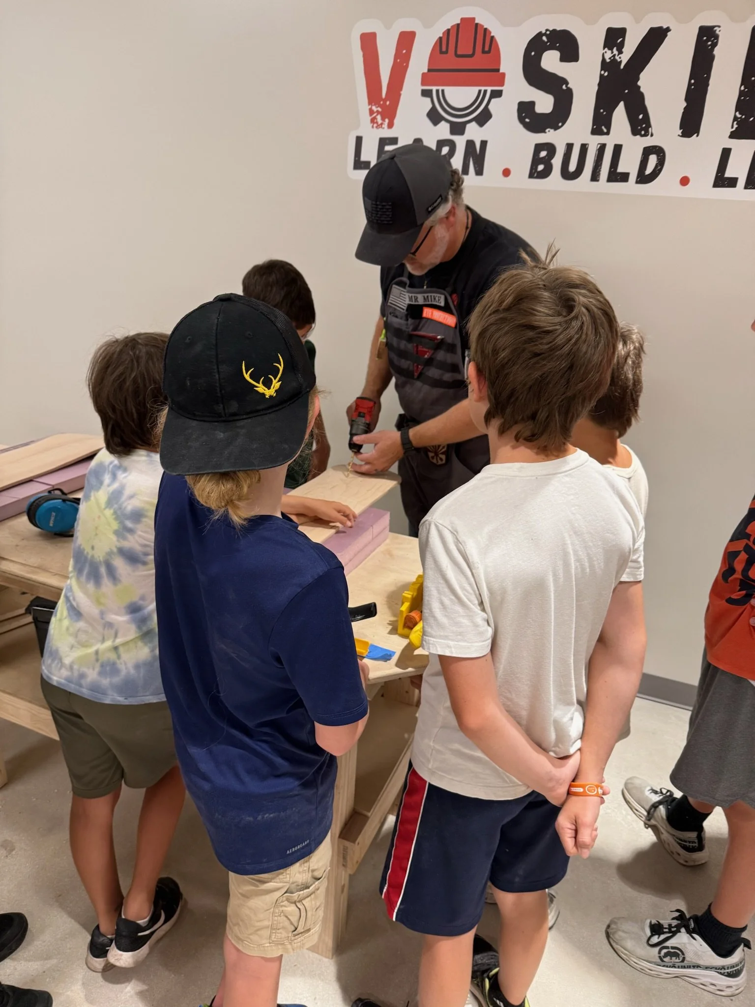 A man shows children how to use a cordless drill during a workshop at a learning center.