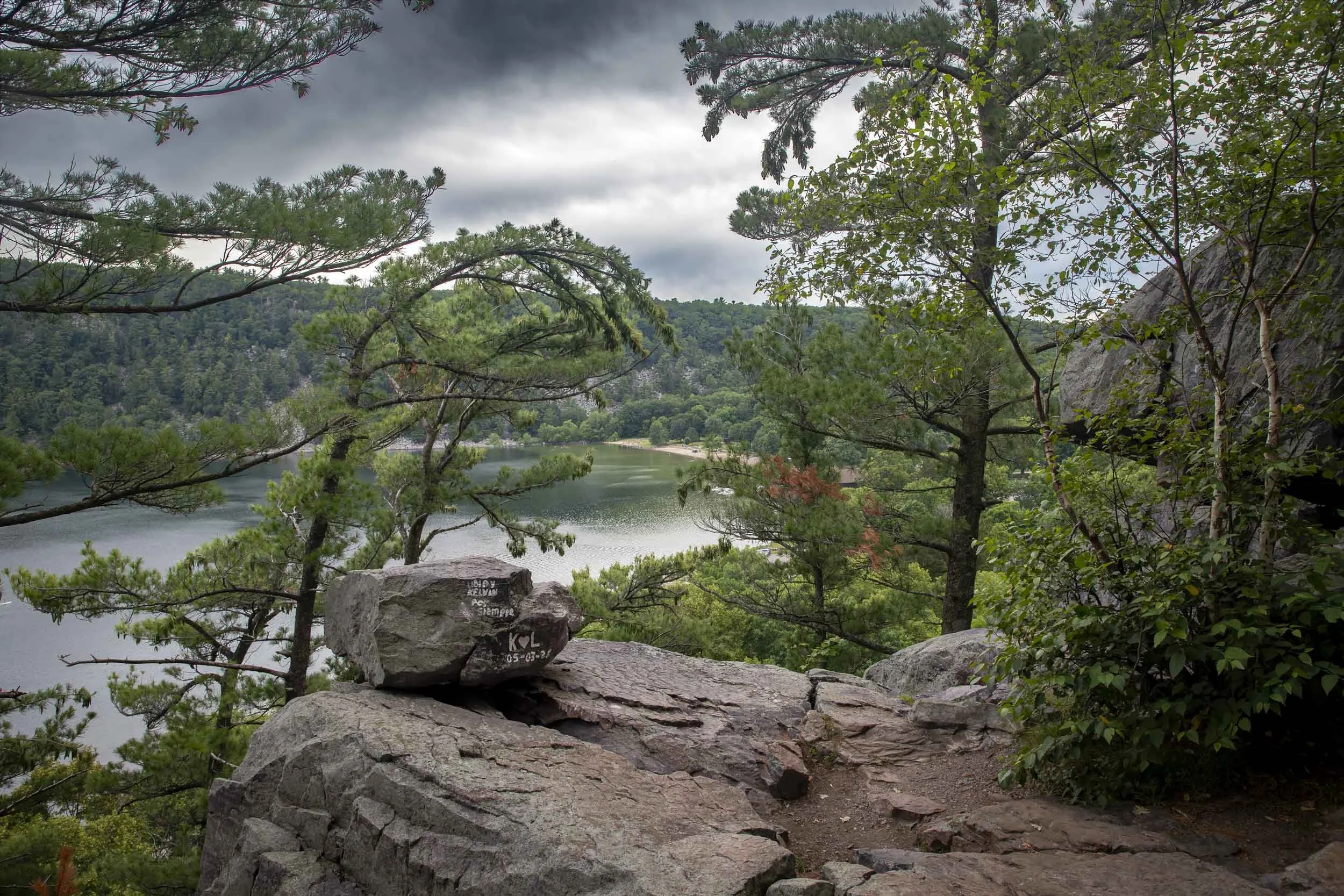 Trees framing a rocky overlook above Devil’s Lake and wooded hills.