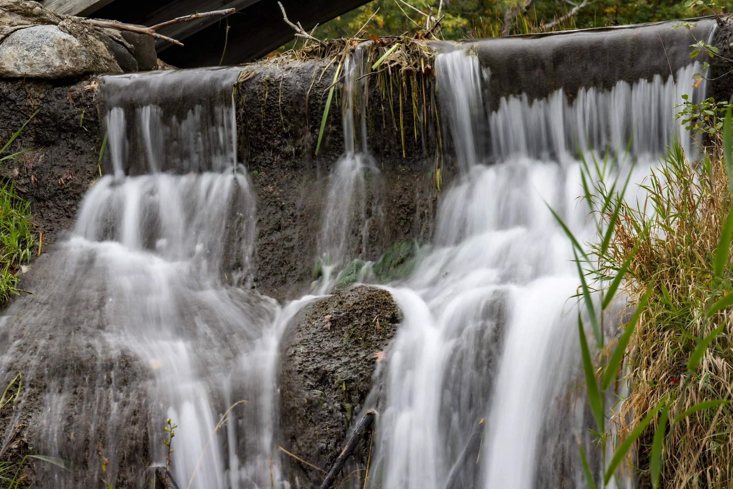 Close-up of water streaming over dark rocks at a small waterfall.