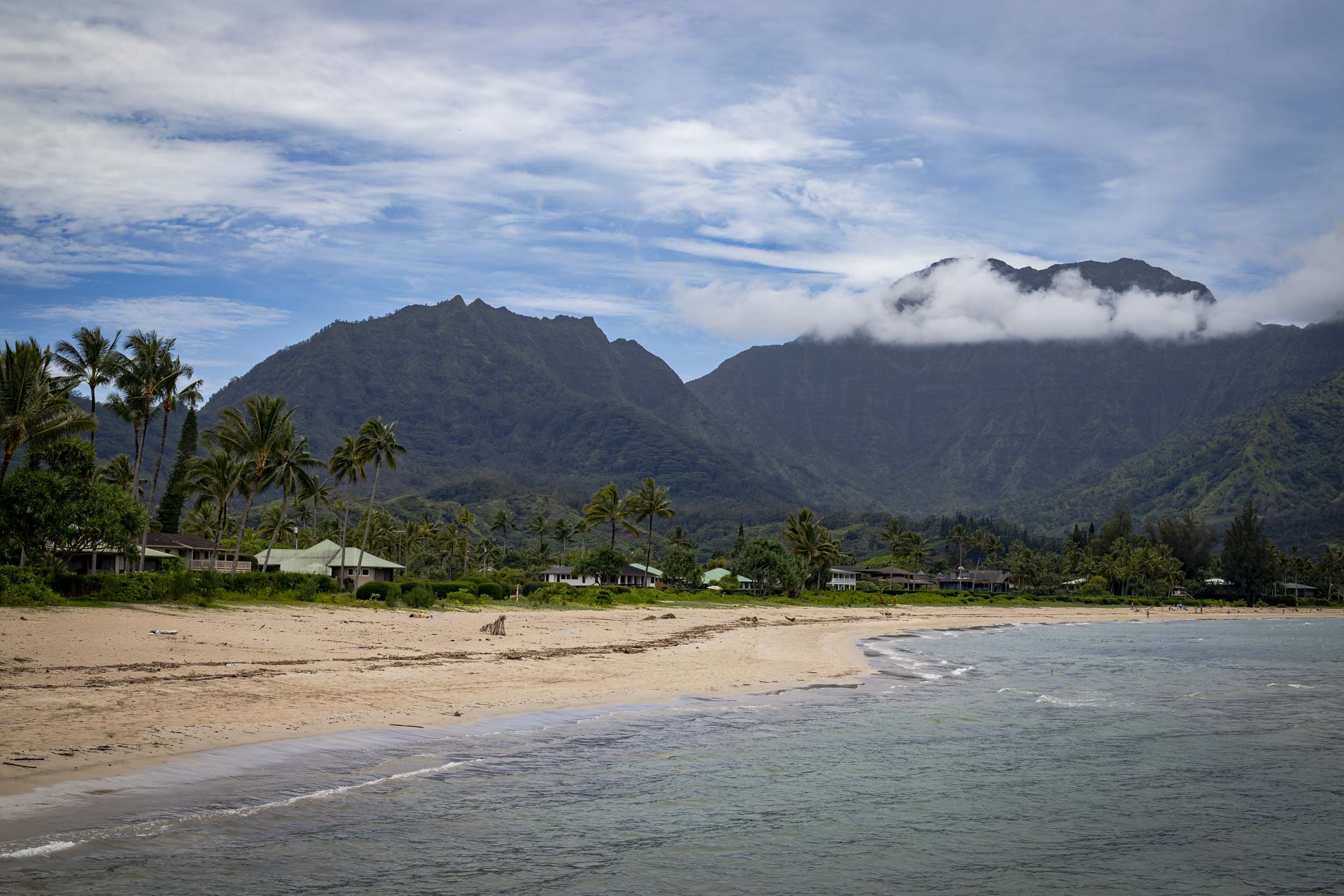 Gentle waves washing onto Hanalei Beach beneath green mountains and low clouds.