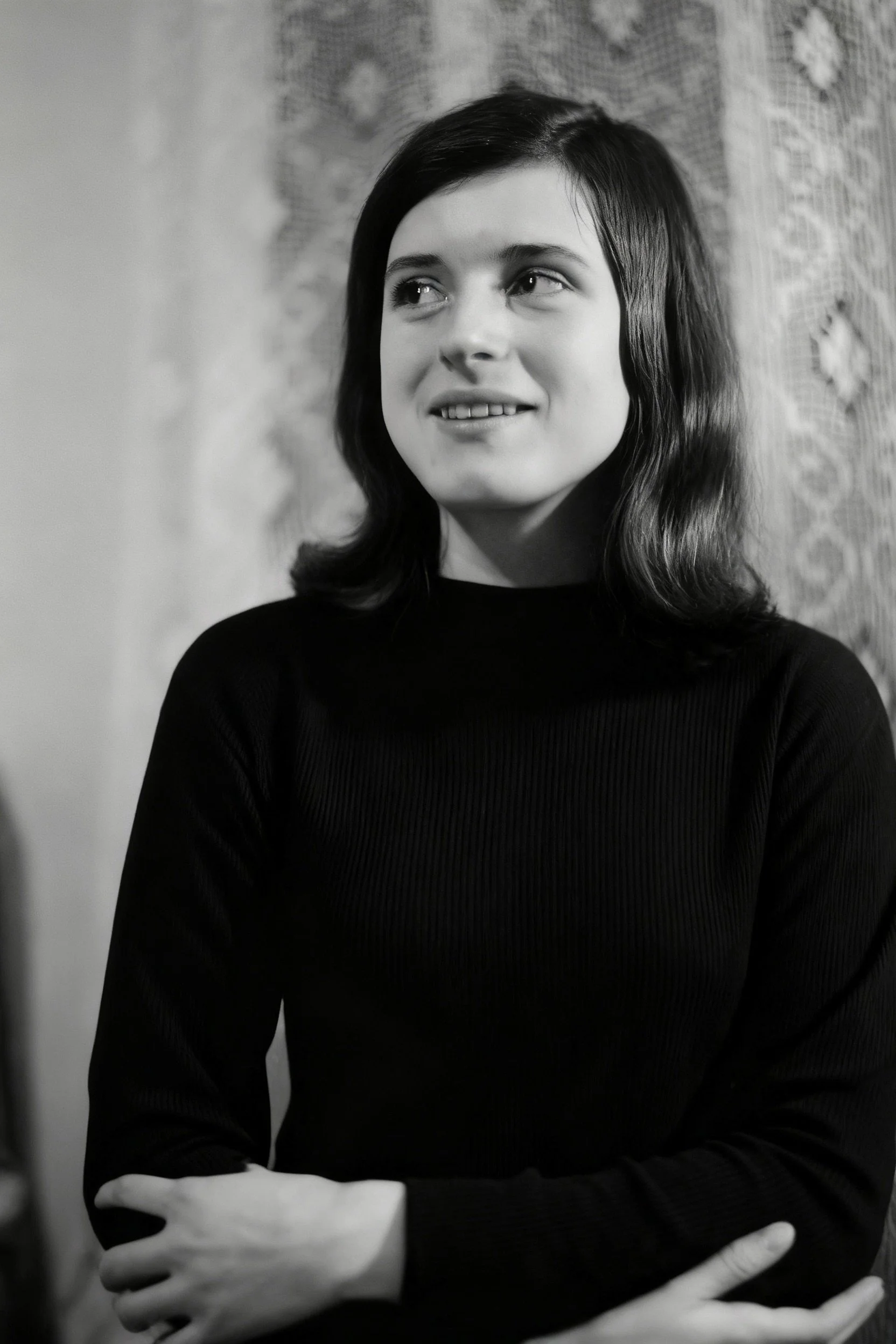 Black-and-white portrait of a smiling young woman in a dark sweater with her arms folded.