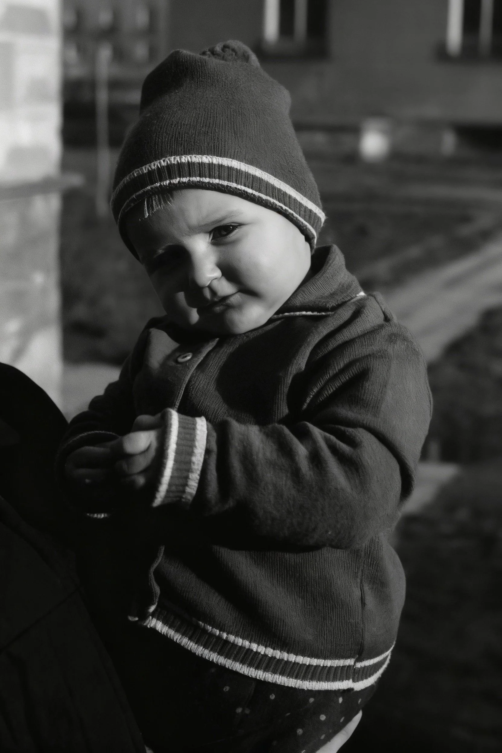 Black-and-white portrait of a small child in a knitted cap and jacket looking down.