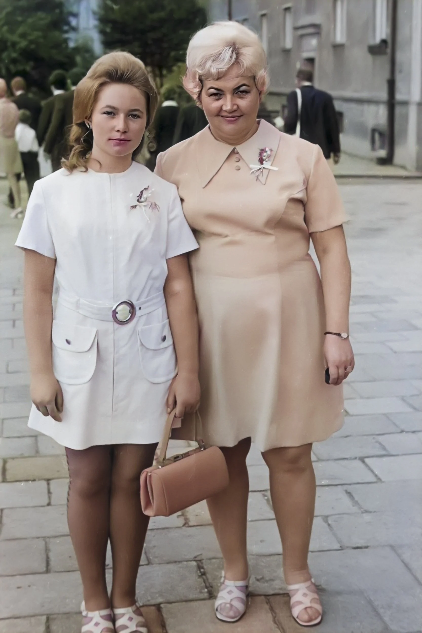 Colorized interpretation of two women standing side by side on a paved street, wearing white and peach dresses.